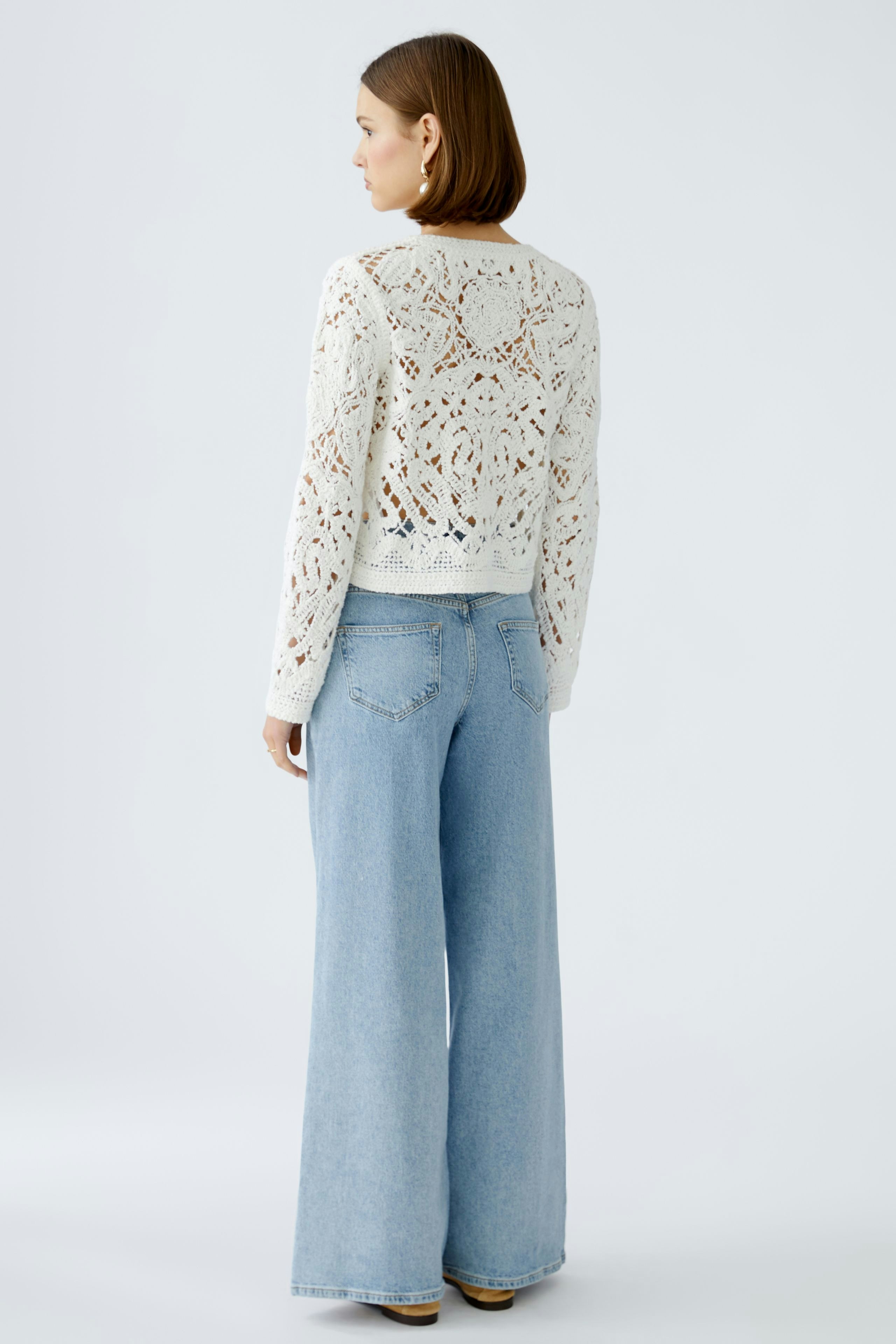 Stylish women's cardigan: A woman in a white knitted cardigan paired with wide-leg jeans.