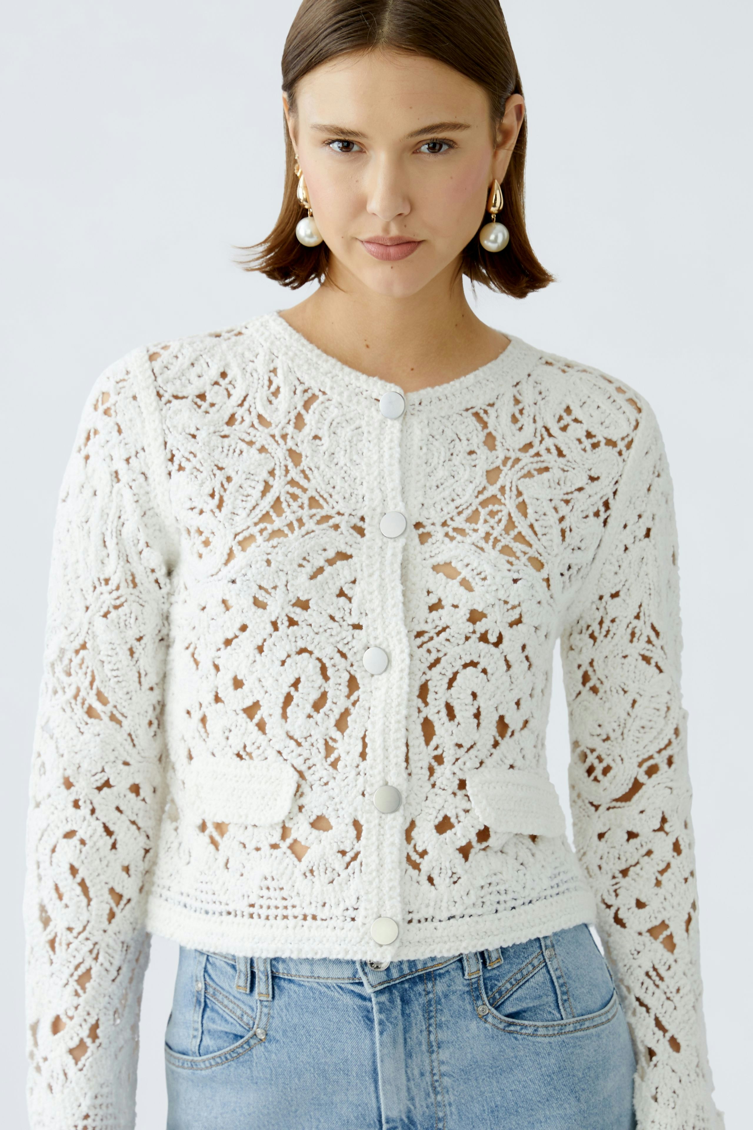Stylish women's cardigan: A woman in a white lace cardigan with buttons and pockets, paired with jeans.