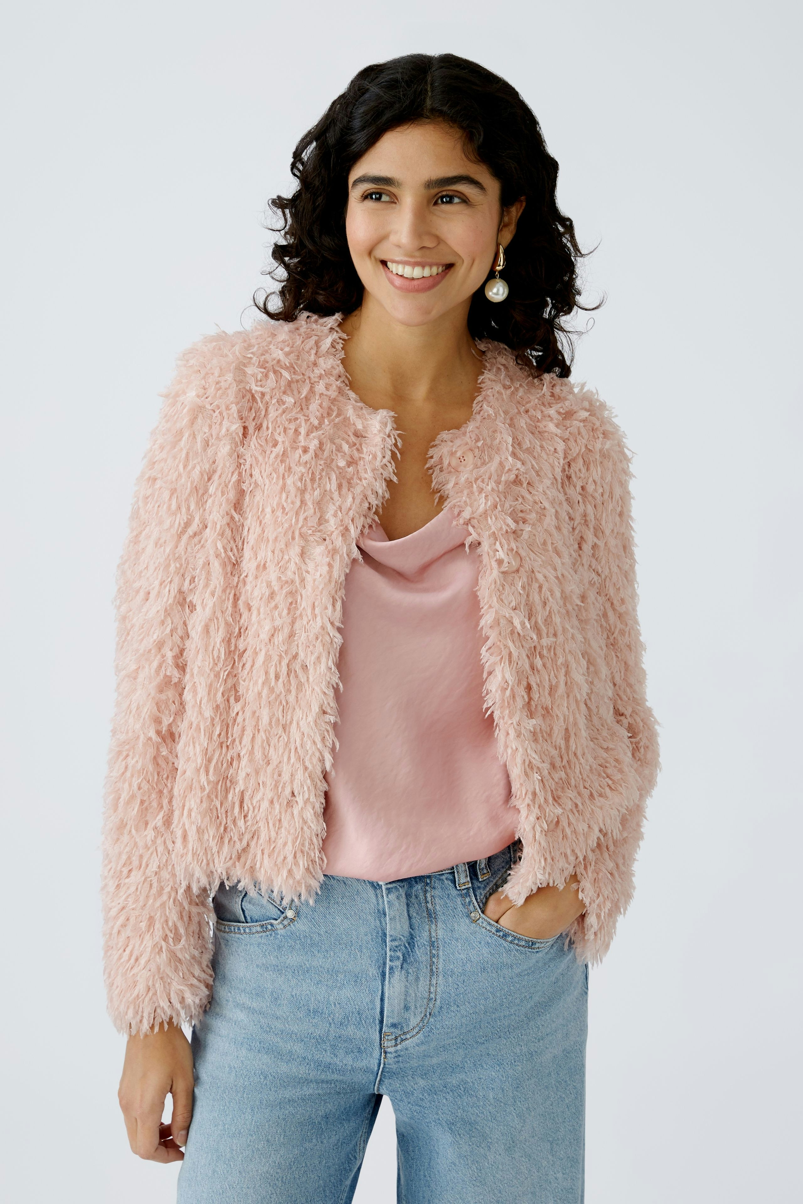 Stylish women's jacket: A woman in a fluffy pink jacket over a pink top and jeans smiles confidently.