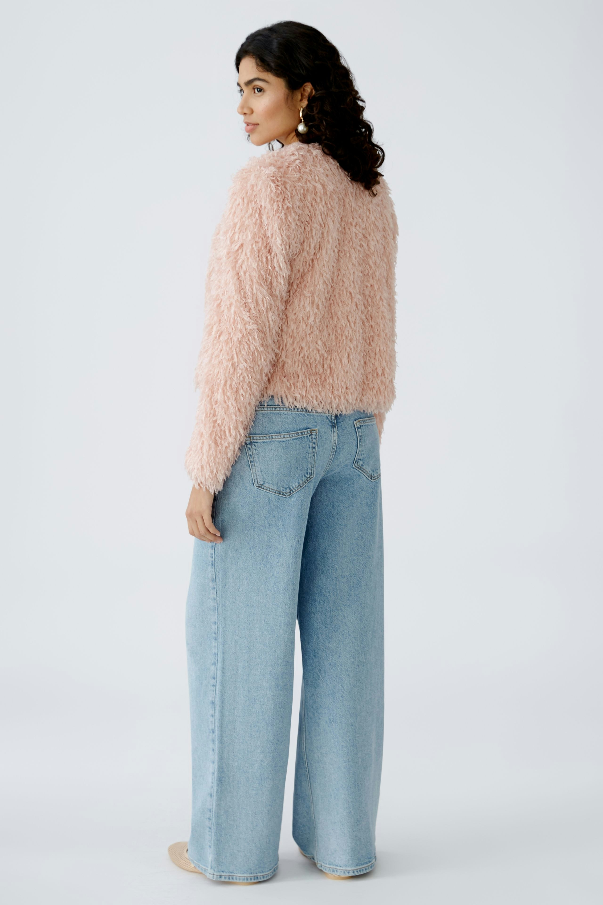 Stylish women's jacket: A woman in a fluffy pink jacket paired with wide-leg jeans, showcasing a trendy look.