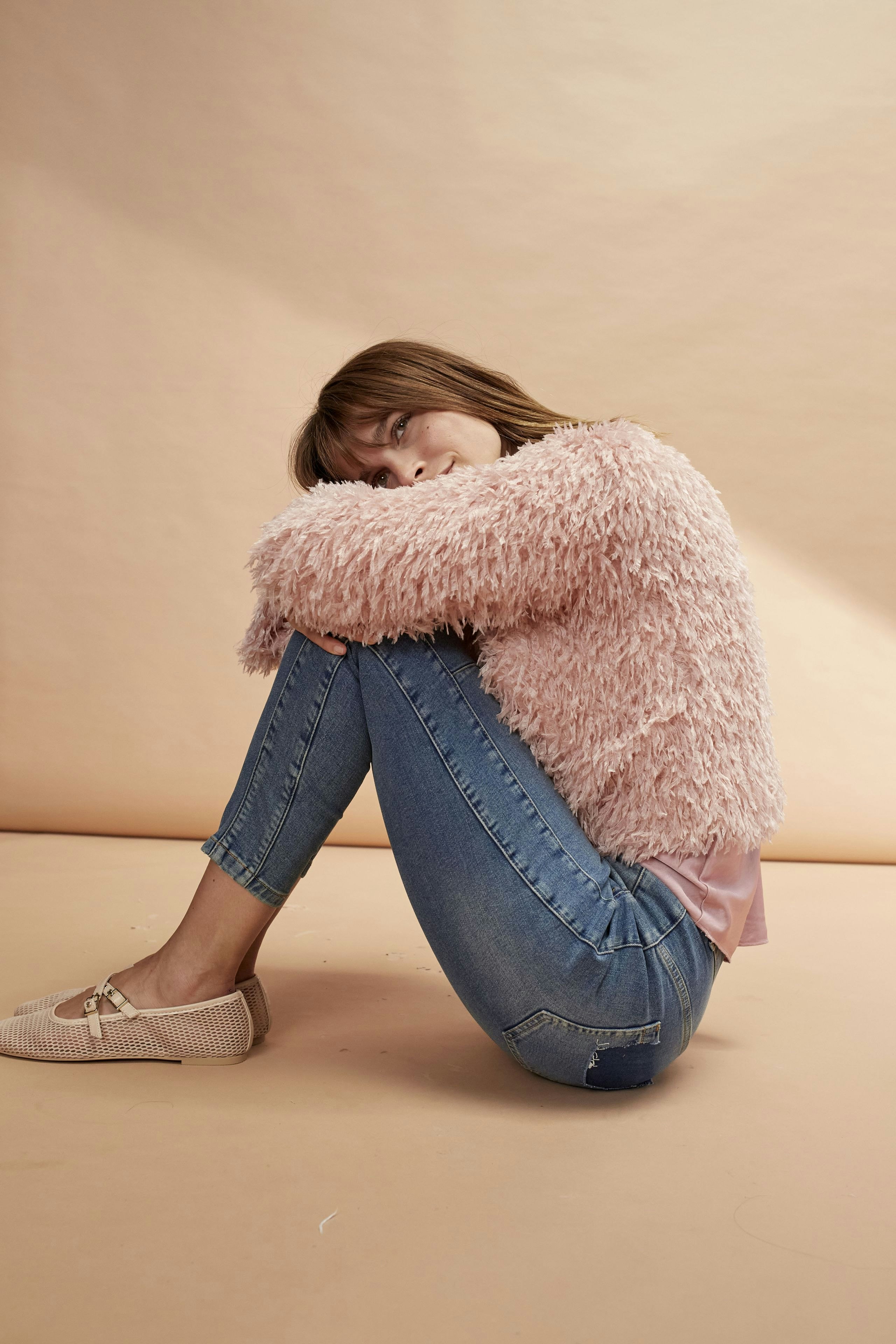 Cozy women's jacket: A woman in a fluffy pink jacket sits comfortably, showcasing a relaxed style.