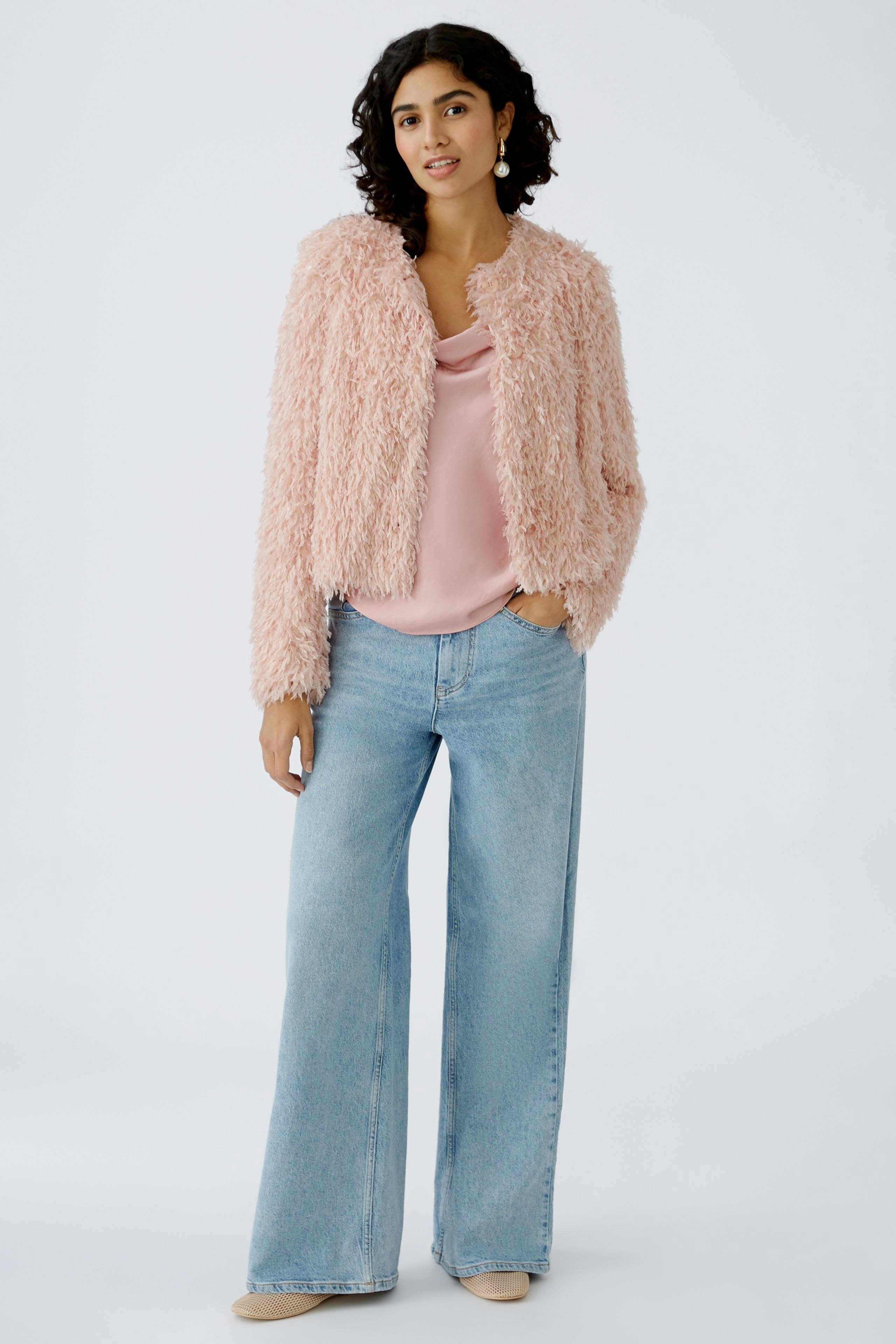 Stylish women's jacket: A woman in a fluffy pink jacket over a pink top and wide jeans.