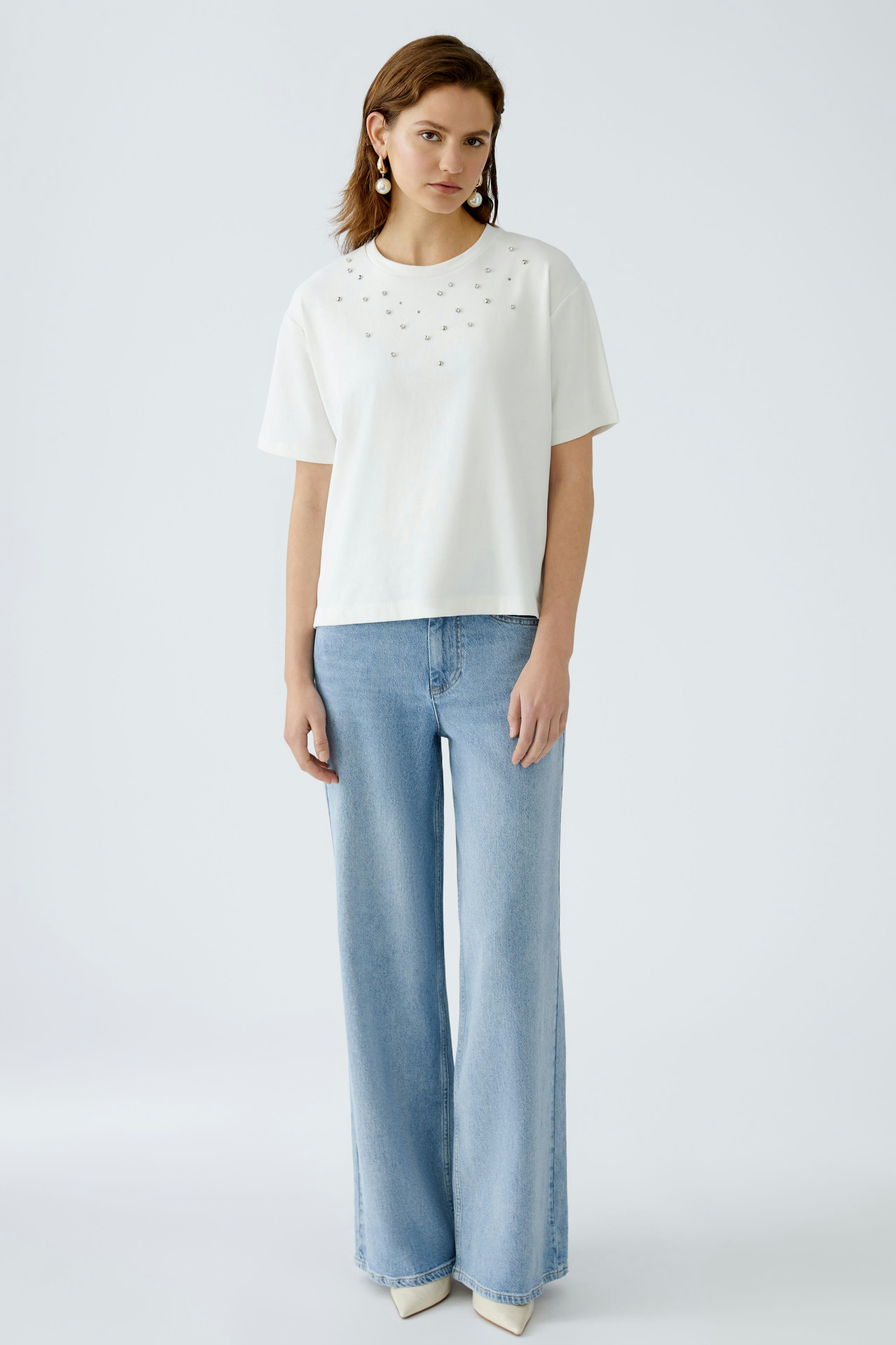 Stylish women's T-shirt: A woman in a white tee with embellishments, paired with wide-leg jeans.