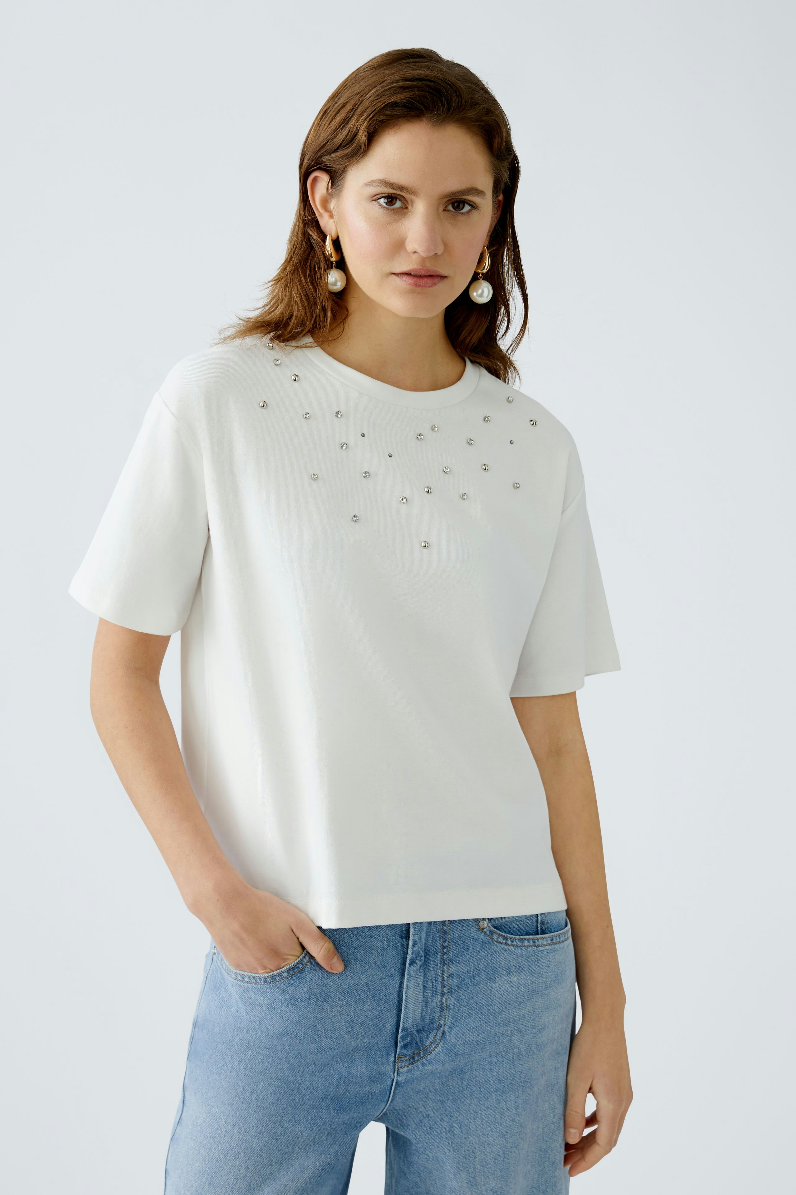 Stylish women's T-shirt: A woman in a white tee adorned with sparkling details, paired with casual jeans.
