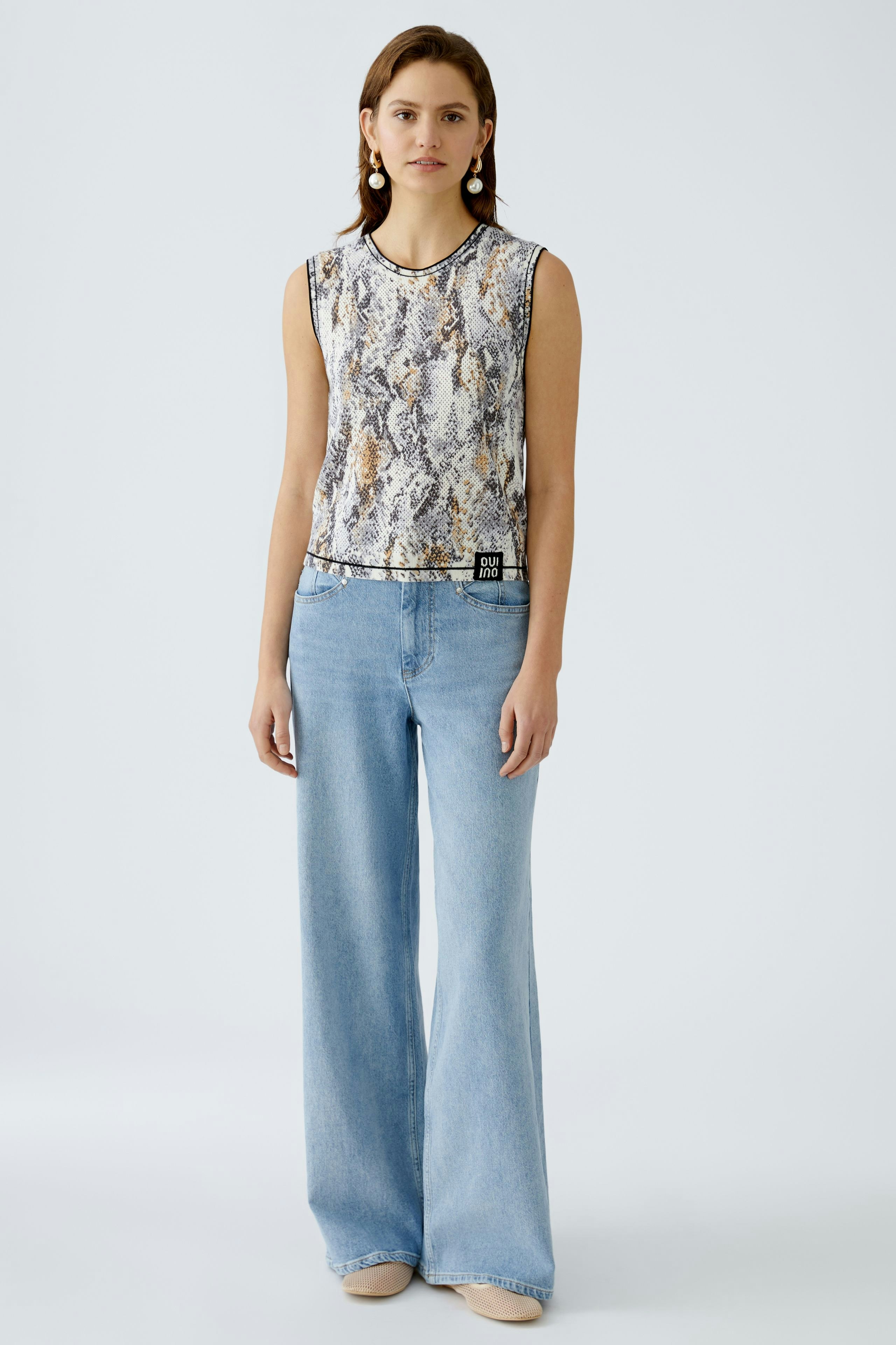 Stylisches Damen-Top: Frau trägt ein ärmelloses Oberteil mit Schlangenmuster und lässigen Jeans.