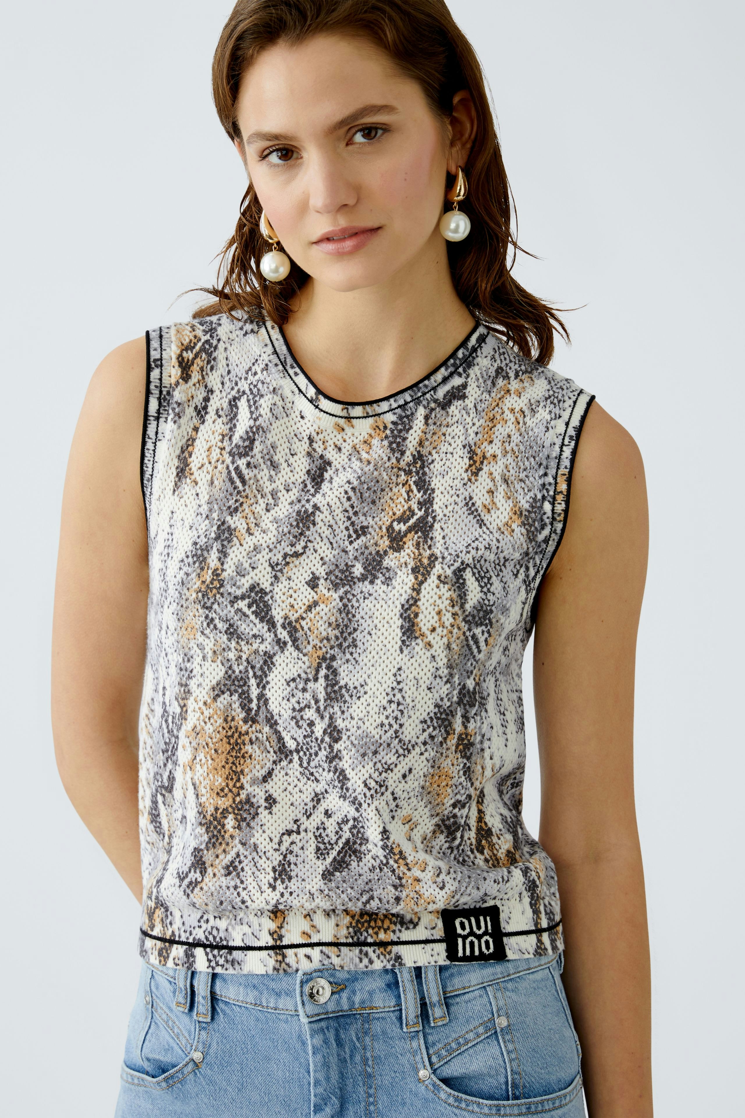 Stylisches Damen-Top: Frau trägt ein ärmelloses Oberteil mit Schlangenprint und lässigen Jeans.