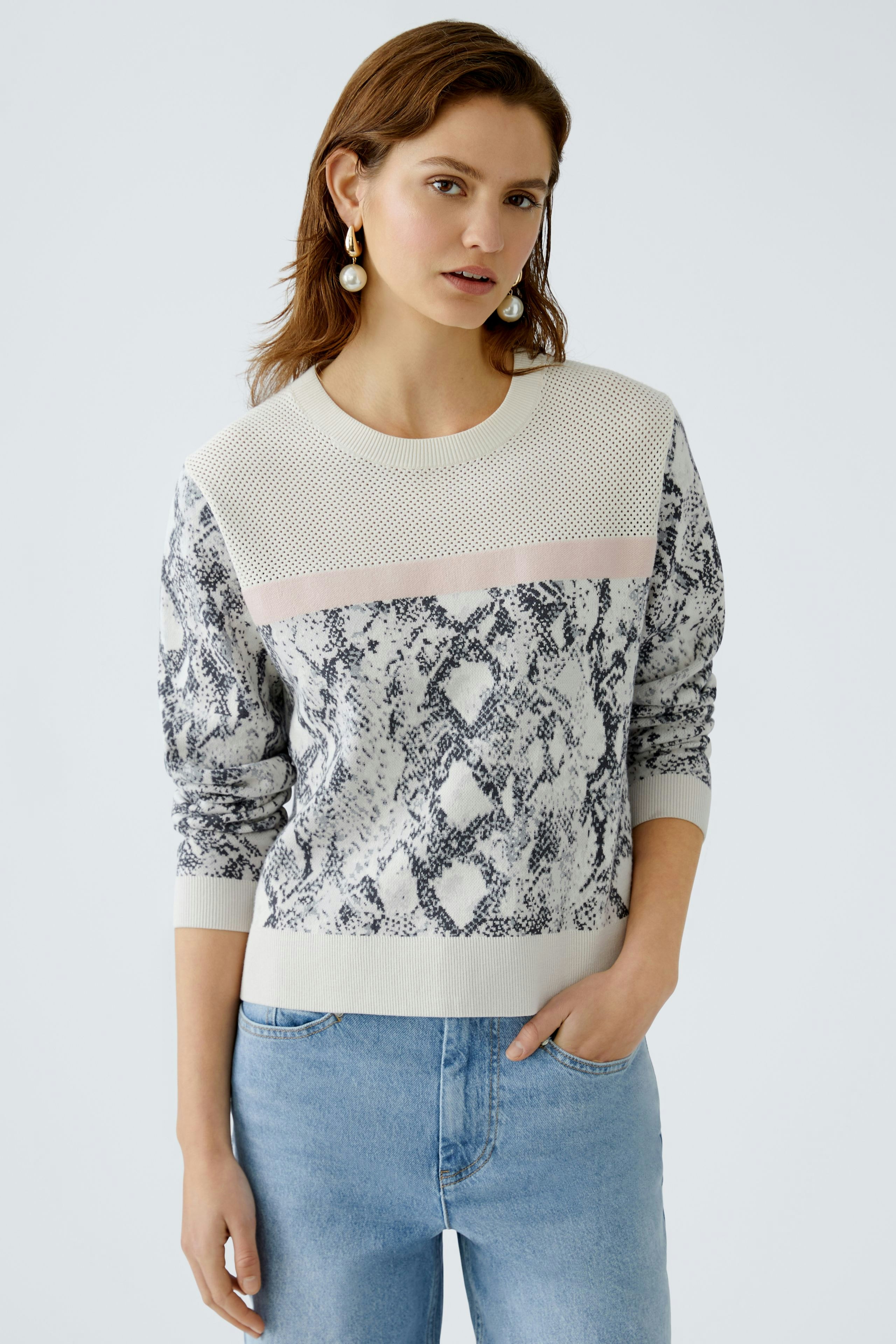 Damen-Pullover: Frau trägt einen modischen Pullover mit Schlangenmuster und sportlichem Design.