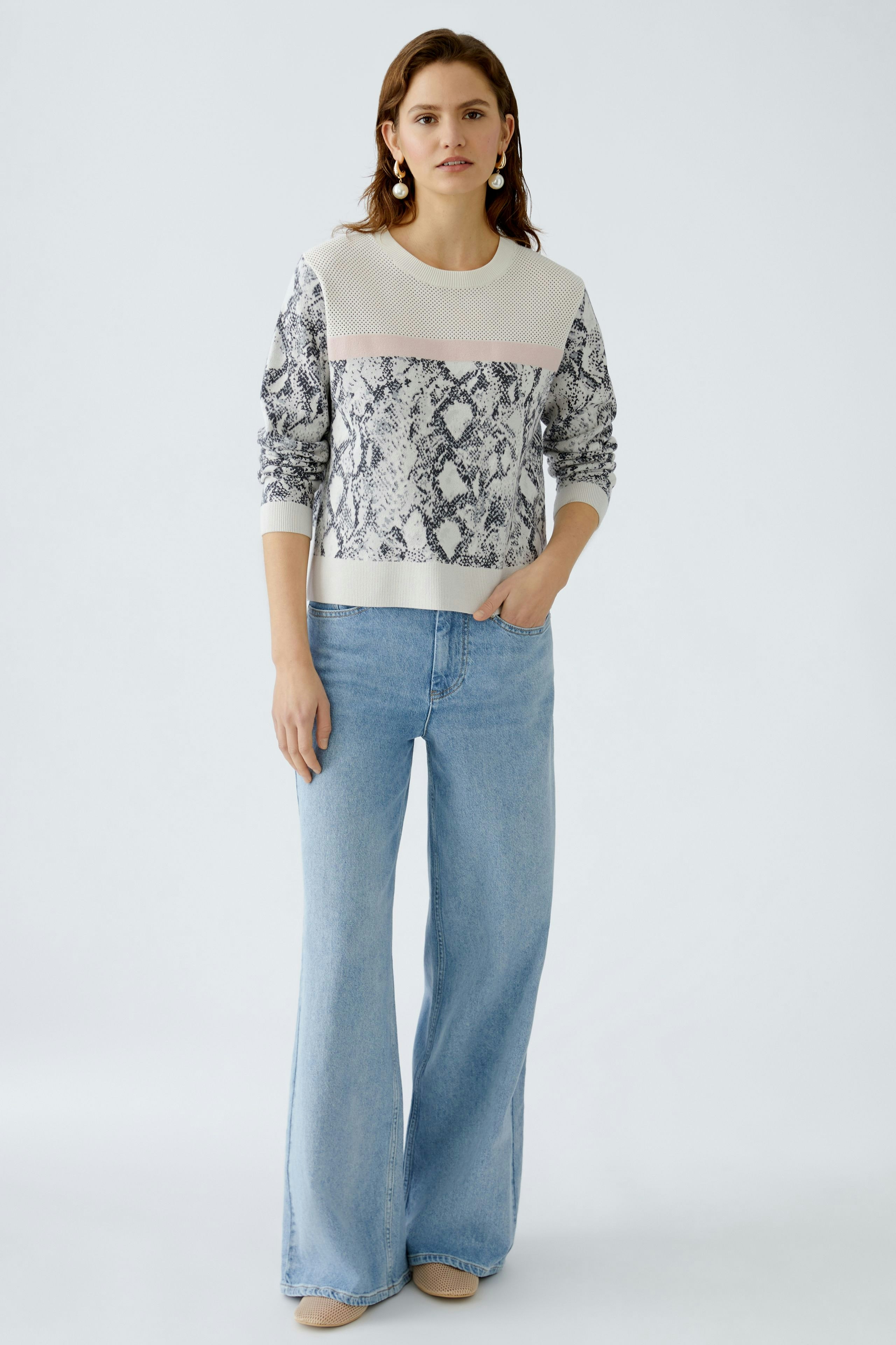 Damen-Pullover: Frau trägt einen modischen Pullover mit Schlangenmuster und lässigen Jeans.