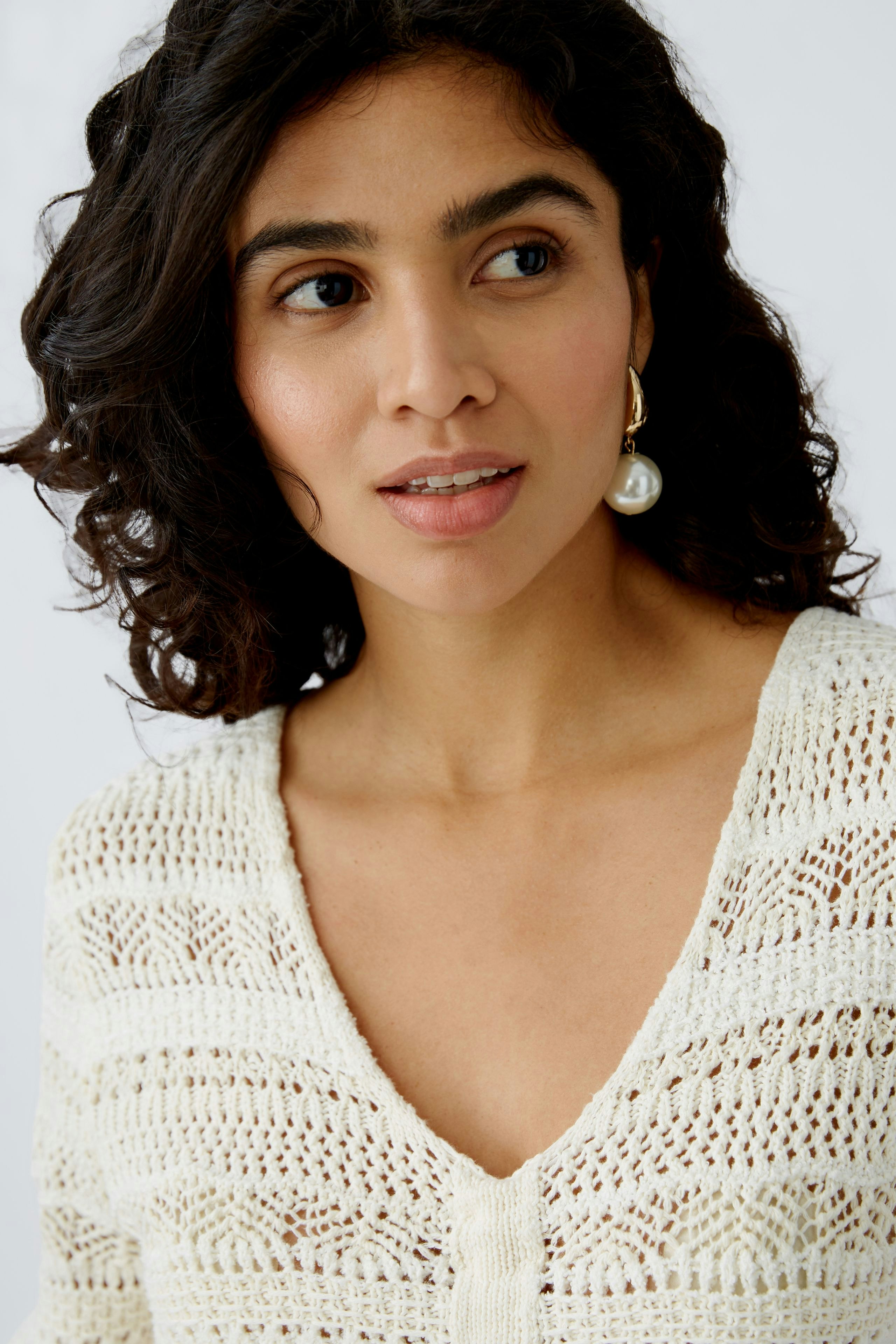 Eleganter Damen-Pullover: Frau mit lockigem Haar trägt einen hellen, luftigen Strickpullover.