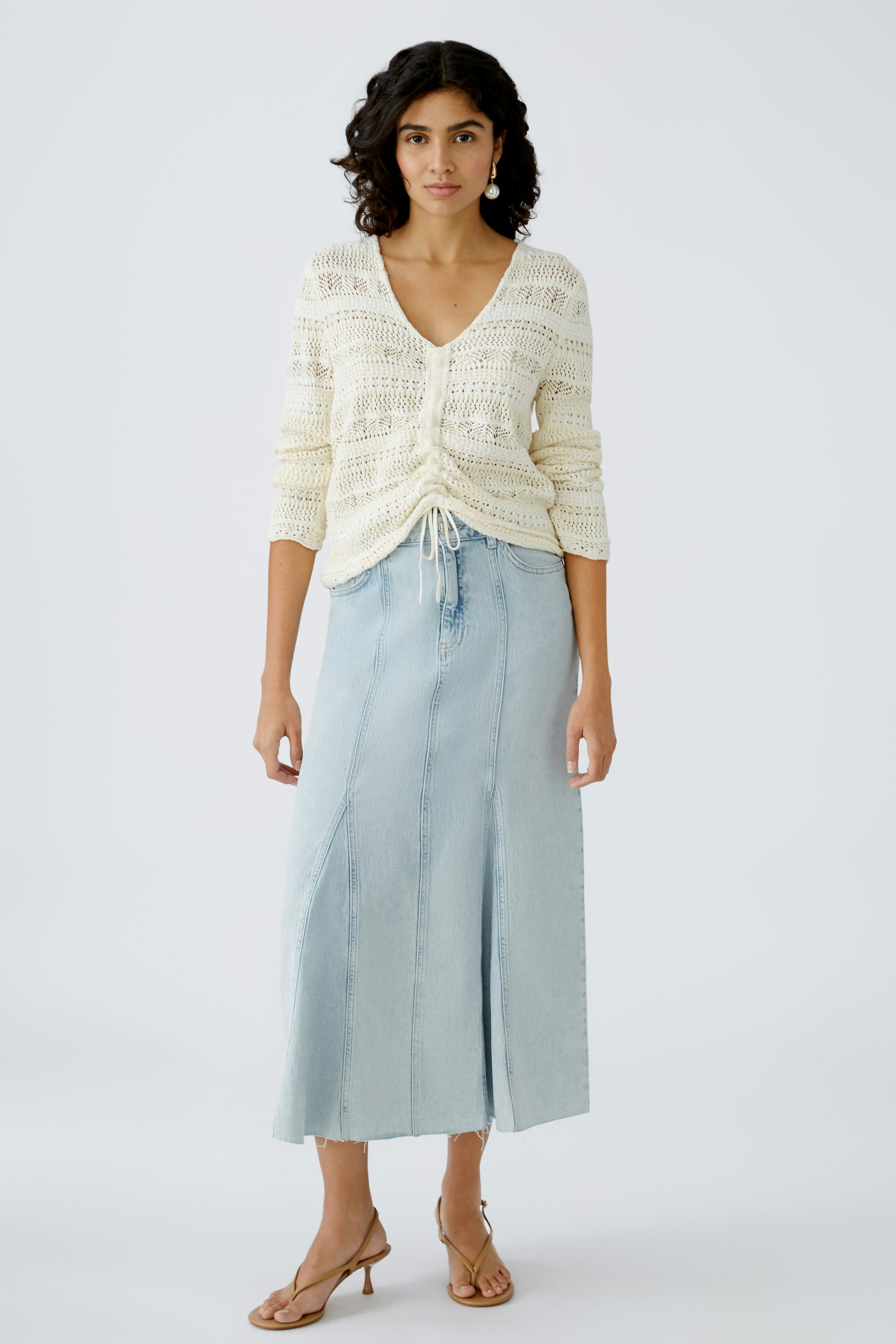 Damen-Pullover: Junge Frau in einem cremefarbenen, lockeren Strickpullover mit Kordelzug.