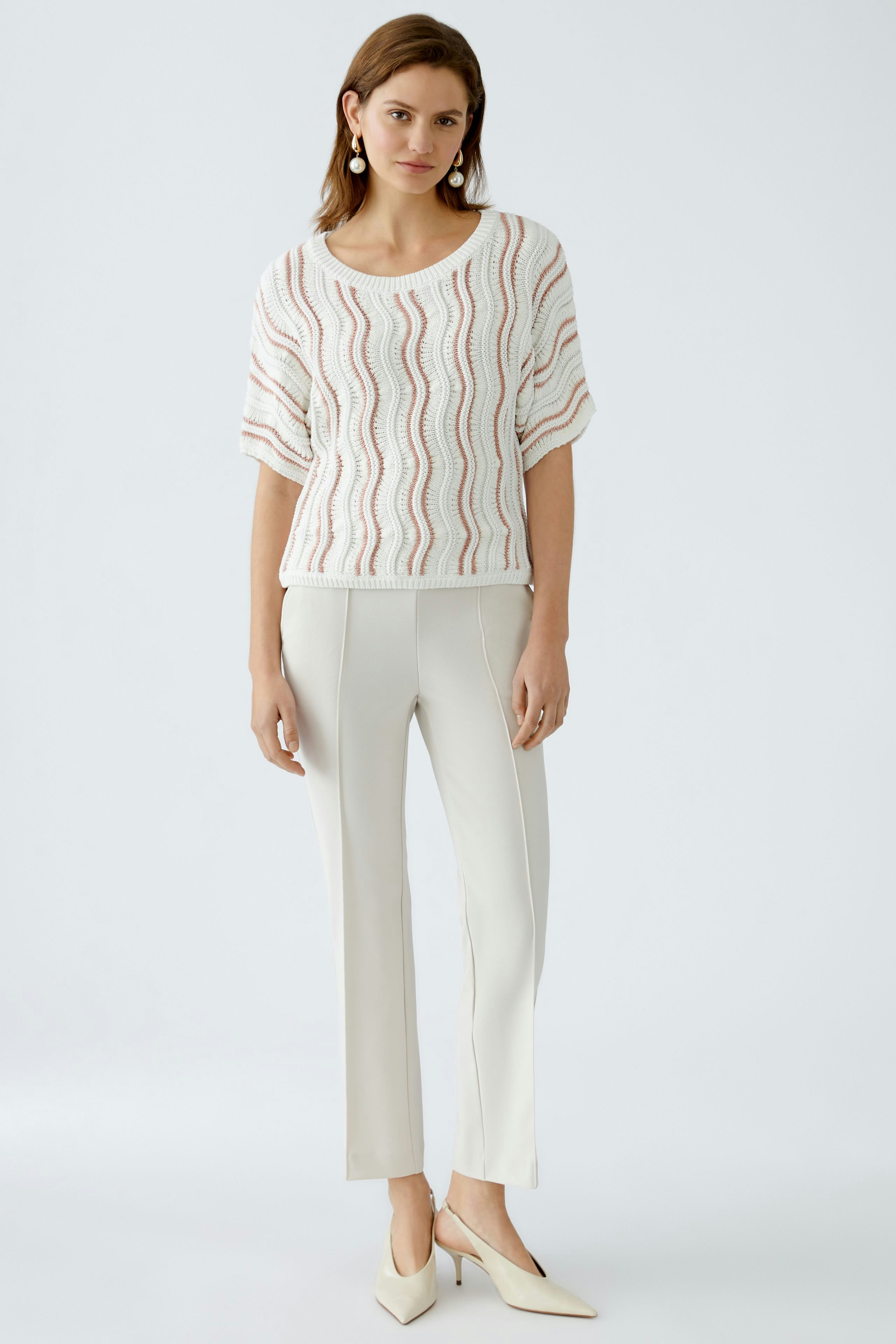 Stylish women's pullover: A woman in a white, wave-patterned pullover paired with light trousers.