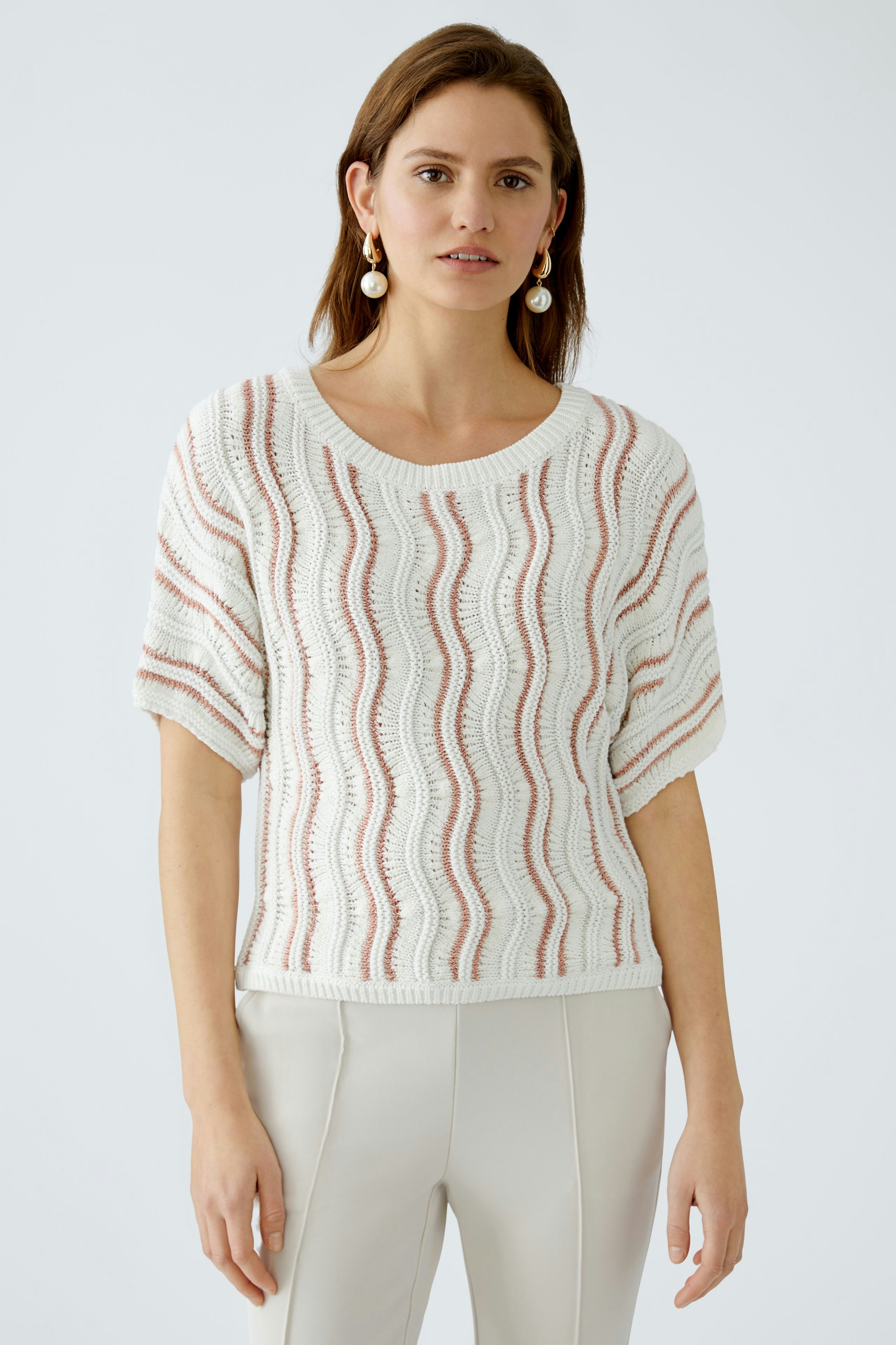 Stylish women's pullover: A woman in a white pullover with wavy patterns, paired with light trousers.
