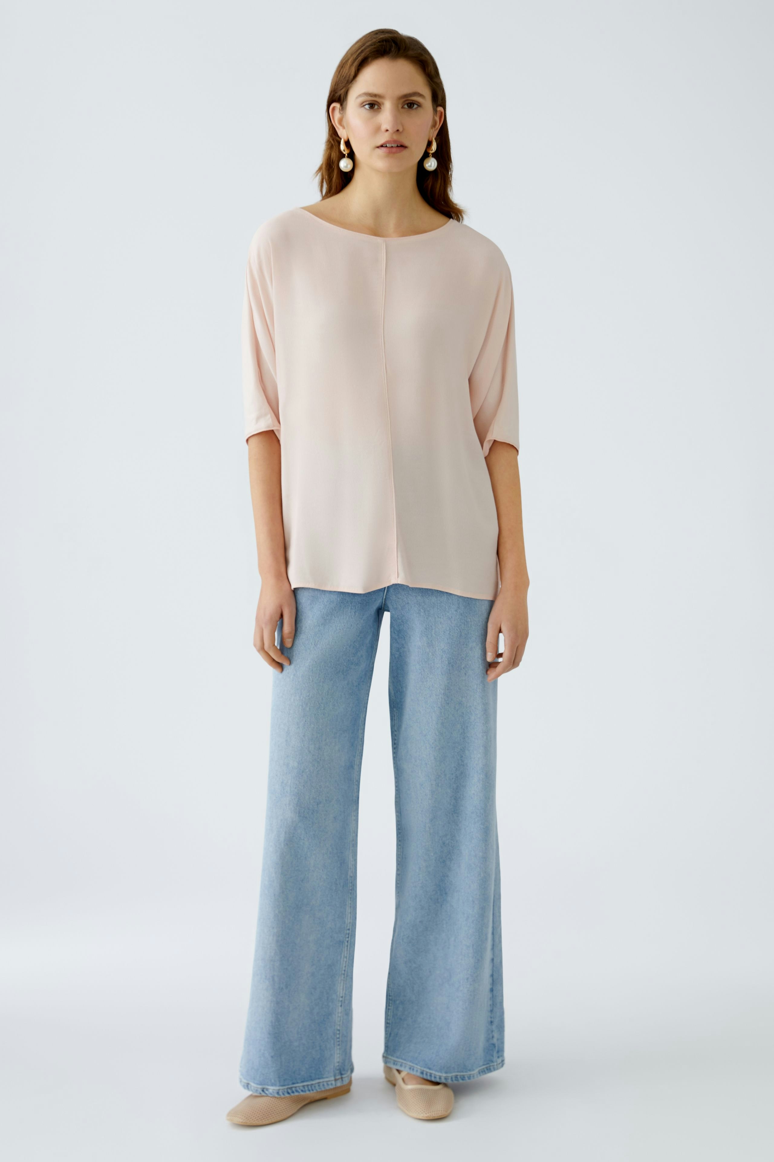 Elegantes Blusenshirt: Junge Frau in einem zarten, rosa Blusenshirt mit lässigen Jeans und eleganten Schuhen.