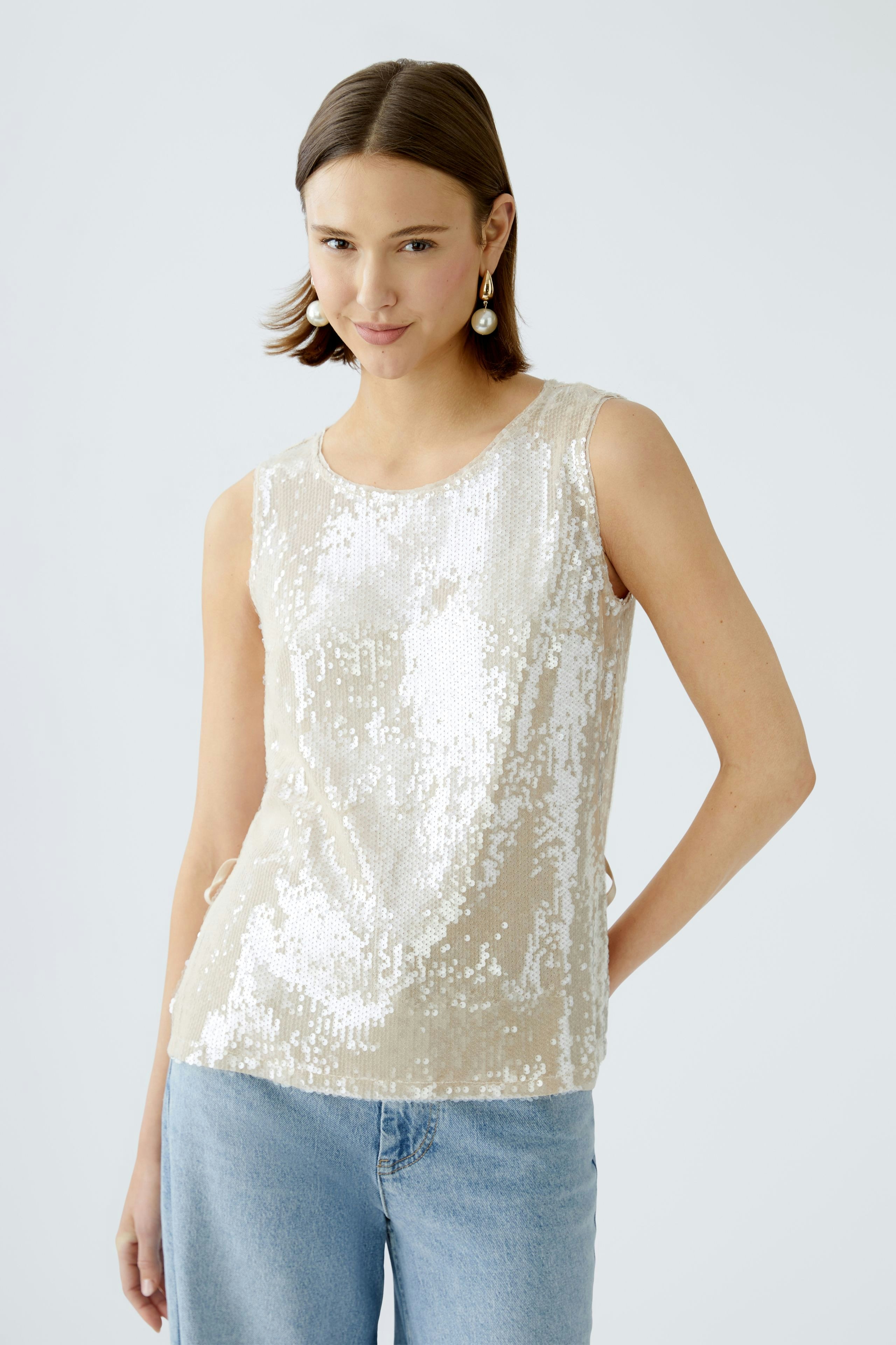 Elegantes Damen-Top: Frau in schimmerndem, beigen Top mit Pailletten und lässigen Jeans.