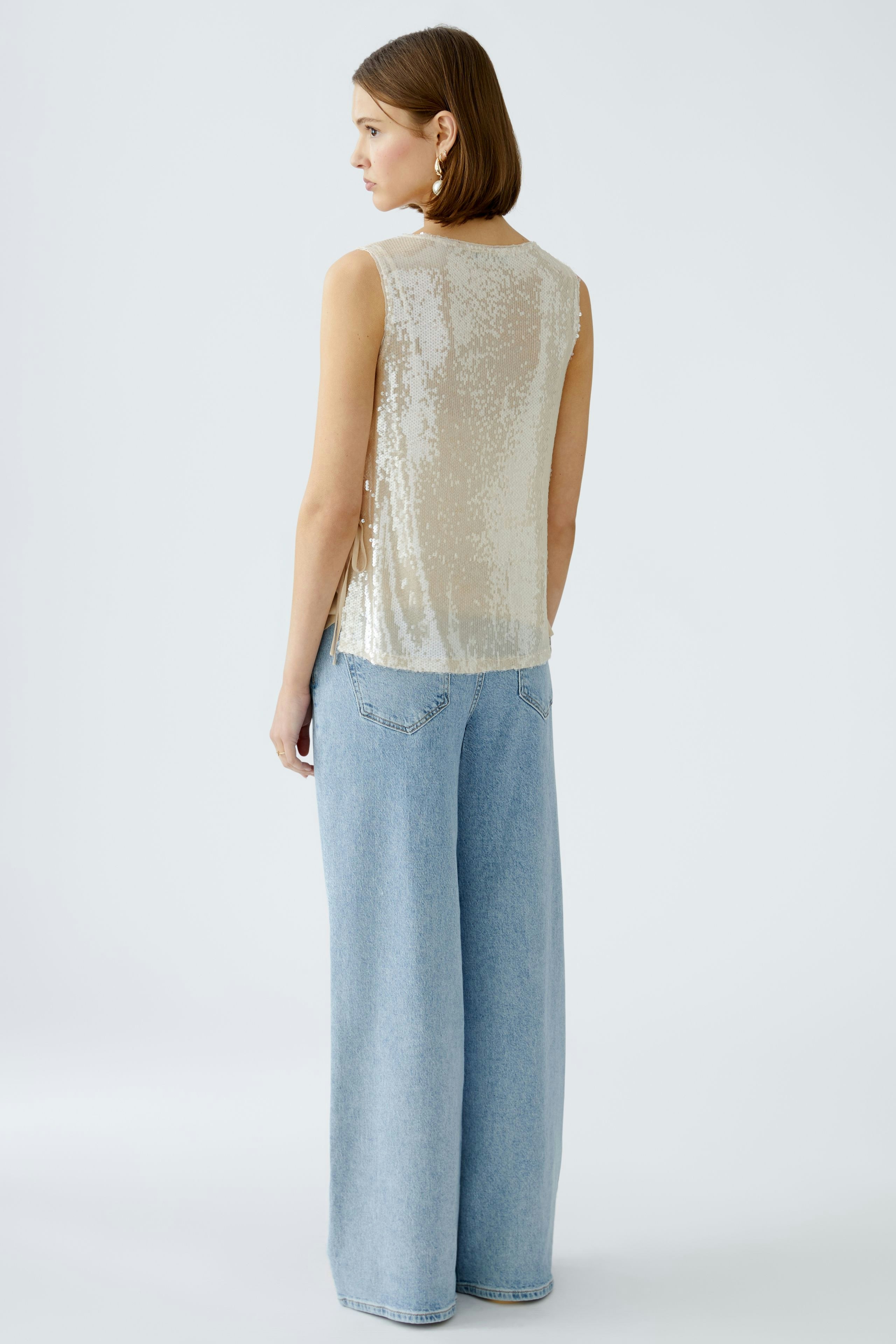 Elegantes Damen-Top: Frau in schimmerndem, ärmellosem Top mit lässigen Jeans von hinten.