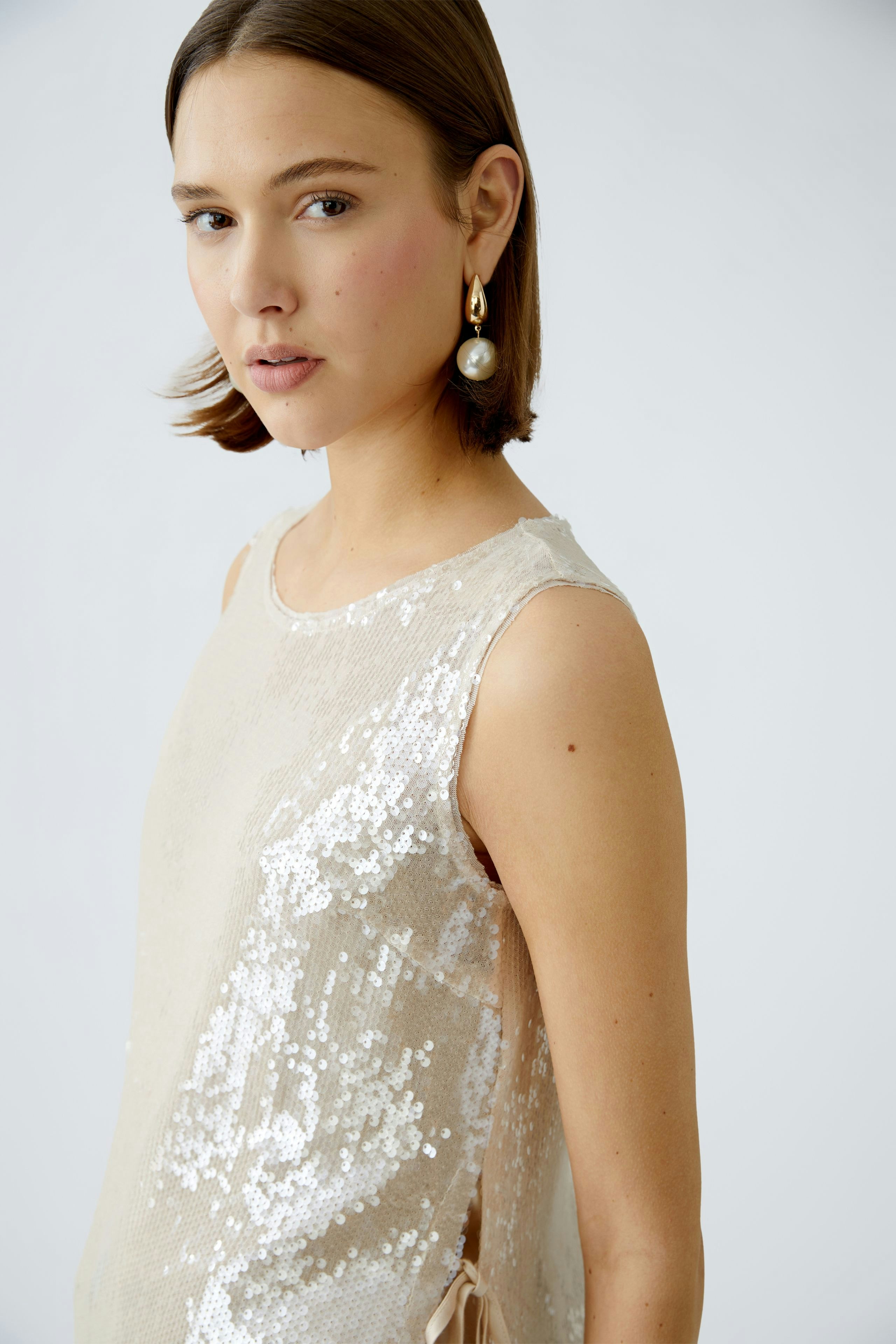 Elegantes Damen-Top: Frau in einem schimmernden, beigen Top mit Pailletten und lässigem Schnitt.