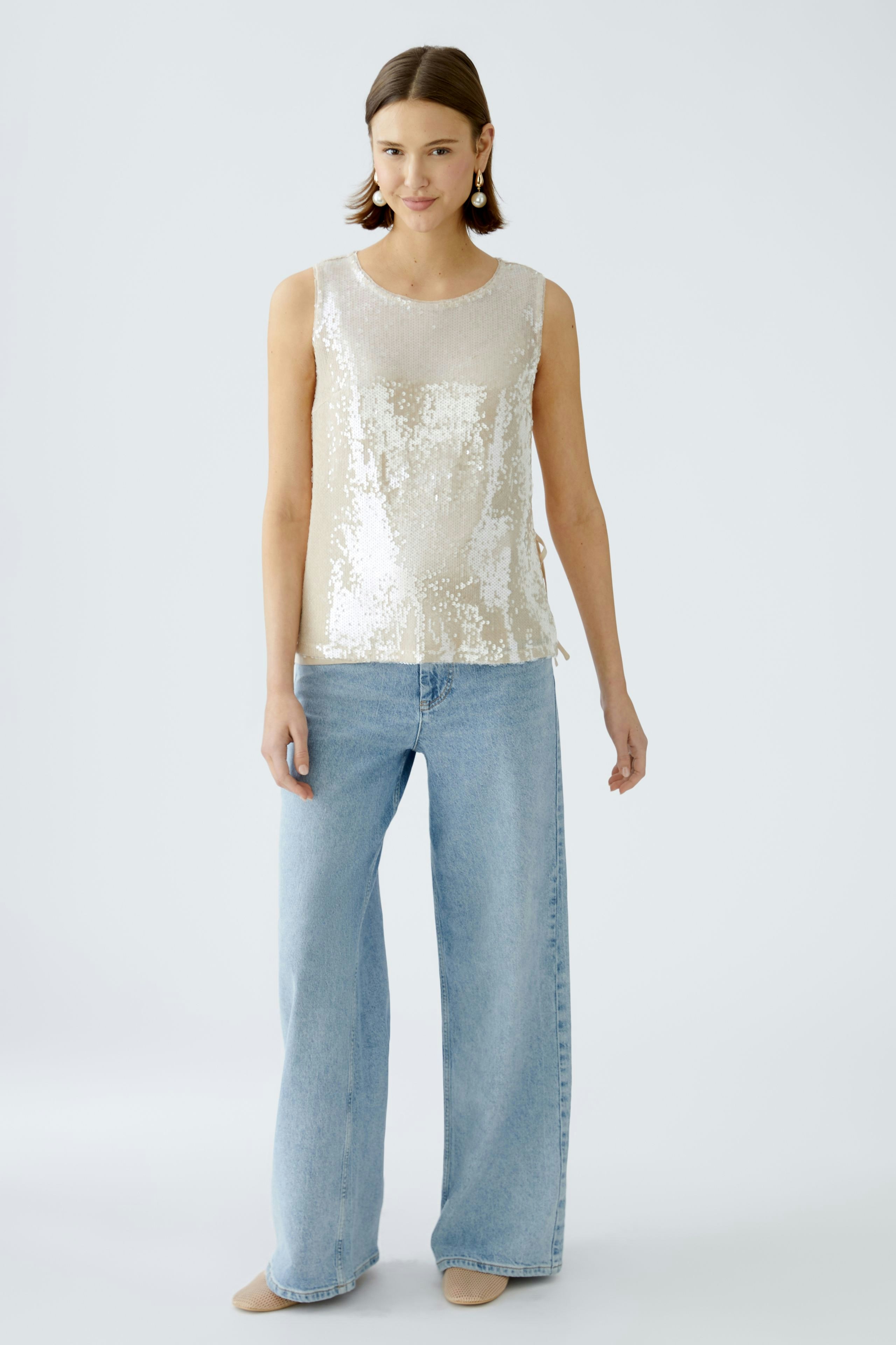 Elegantes Damen-Top: Frau trägt ein schimmerndes, ärmelloses Top mit Pailletten und lässigen Jeans.