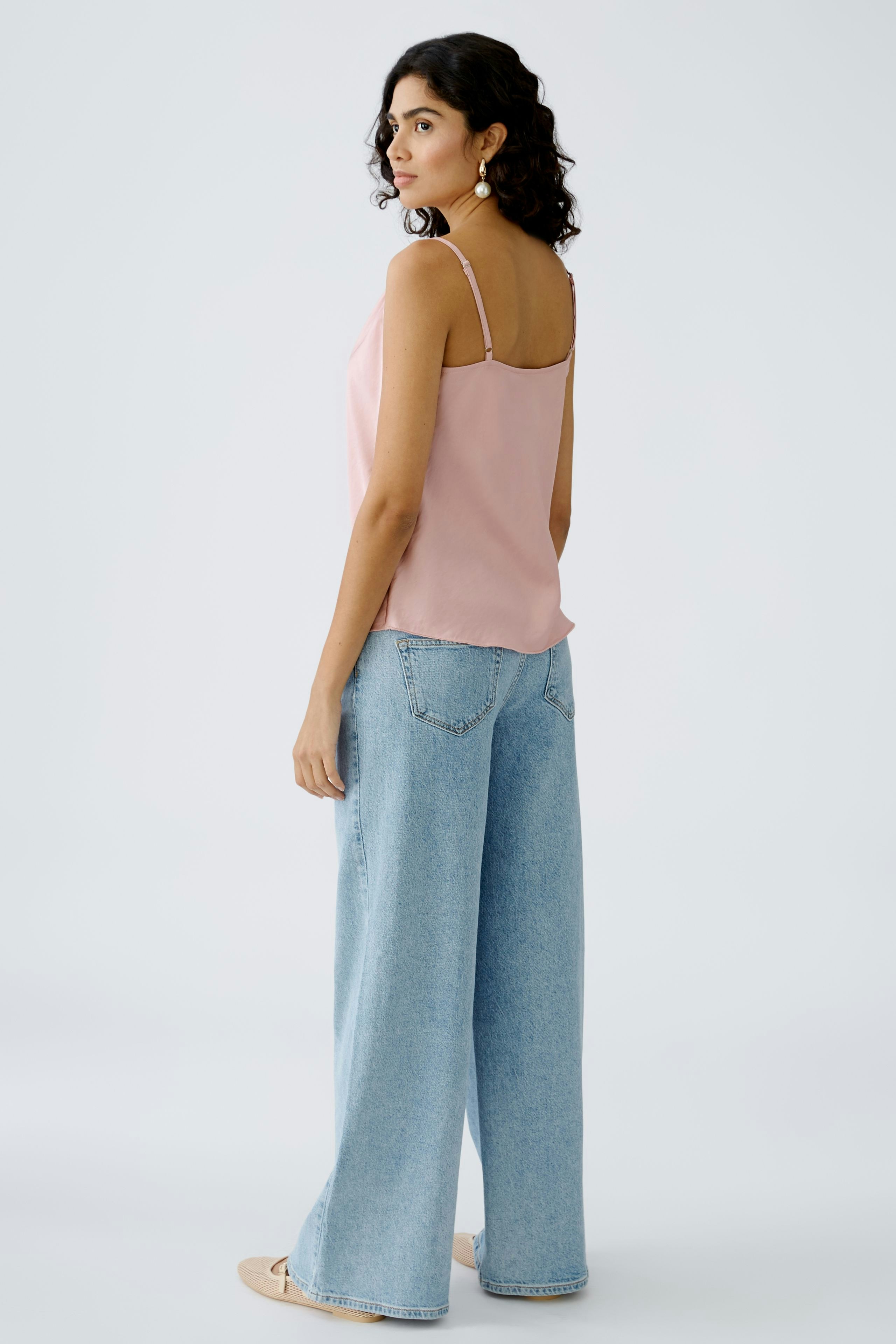 Elegantes Damen-Top: Frau in zartem rosa Top und lässigen Jeans, ideal für einen entspannten Look.