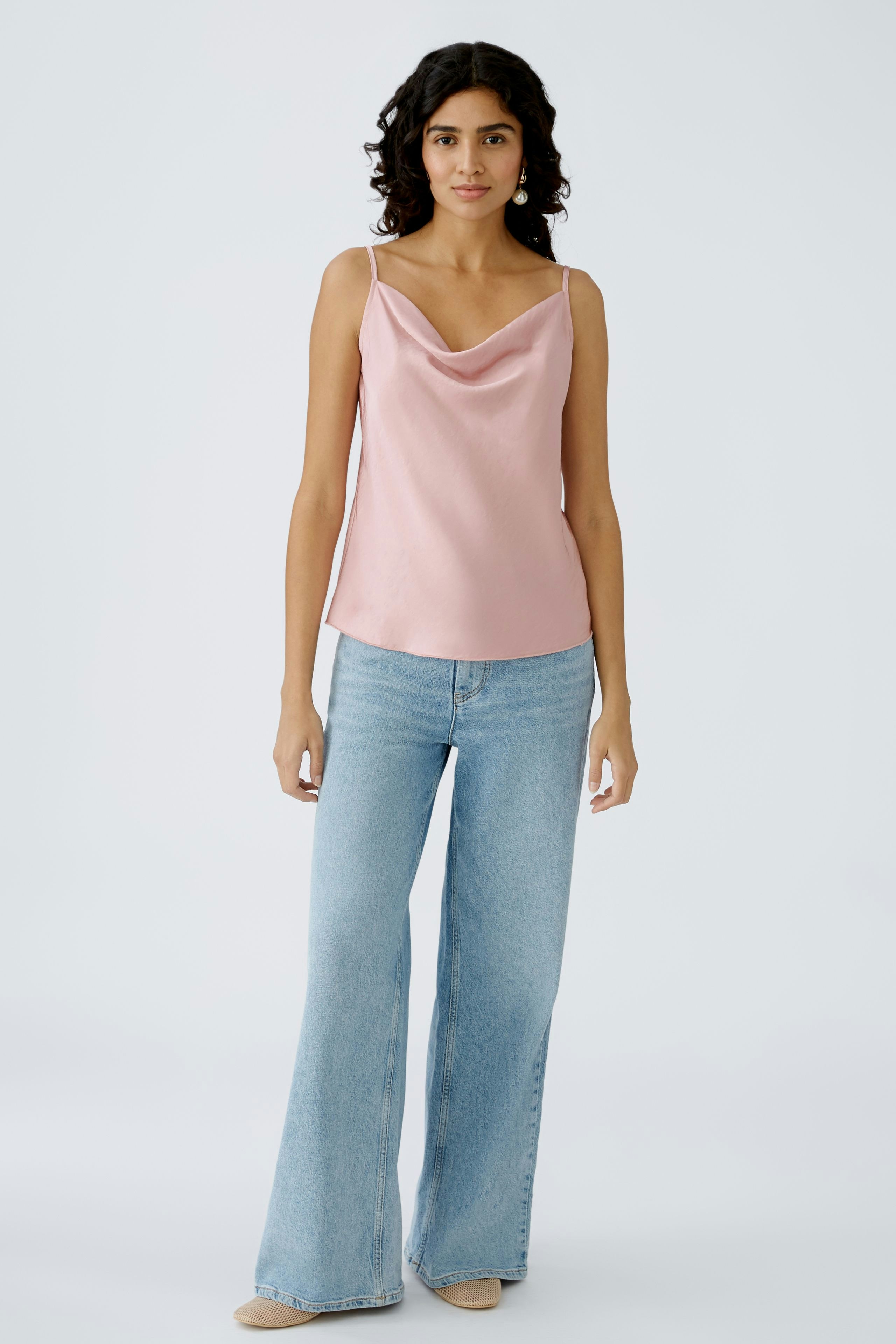 Elegantes Damen-Top: Frau in einem zarten, rosa Top mit schmalen Trägern und lässigen Jeans.