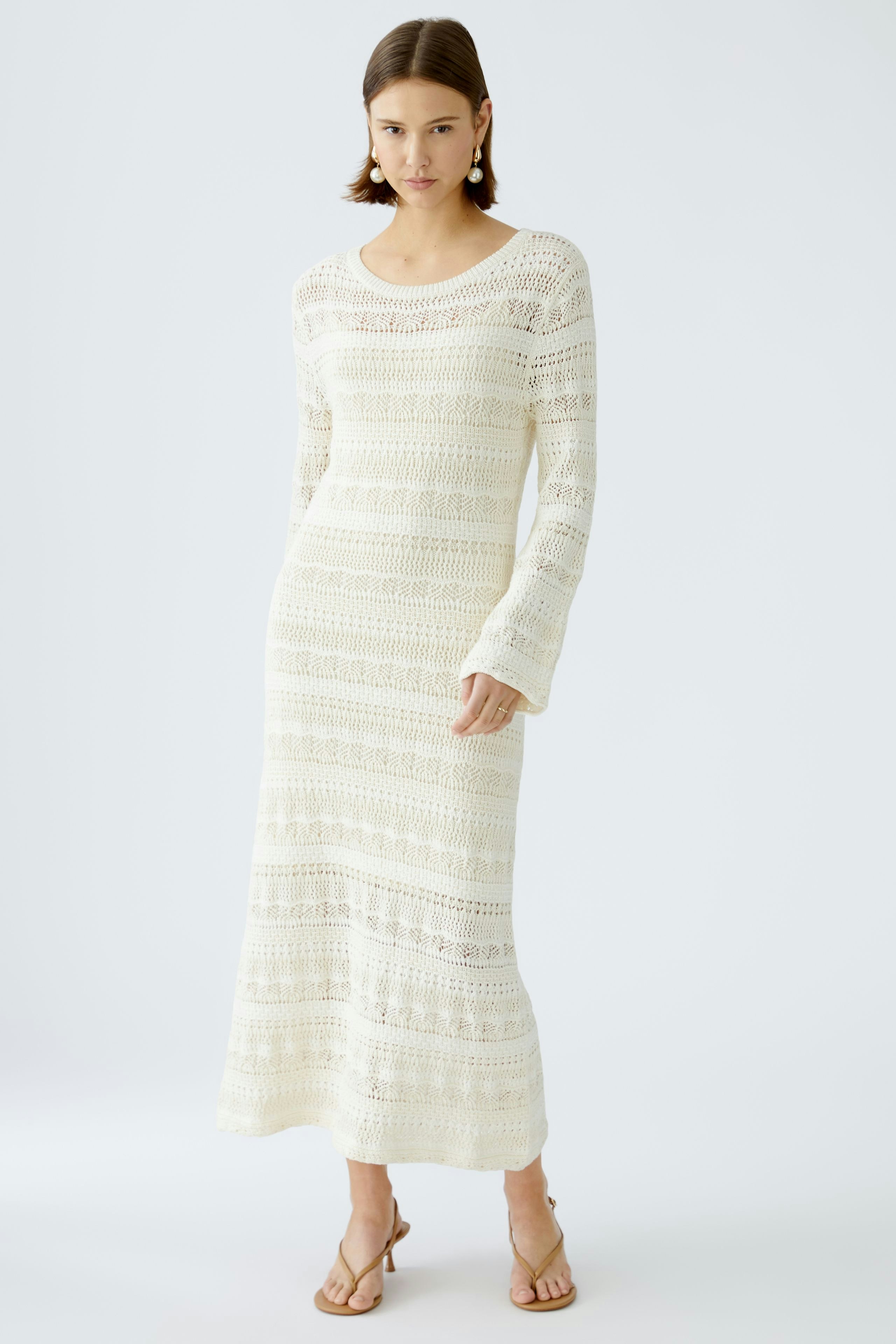 Elegantes Strickkleid: Frau in einem langen, weißen Strickkleid mit feinen Mustern und lässigem Schnitt.