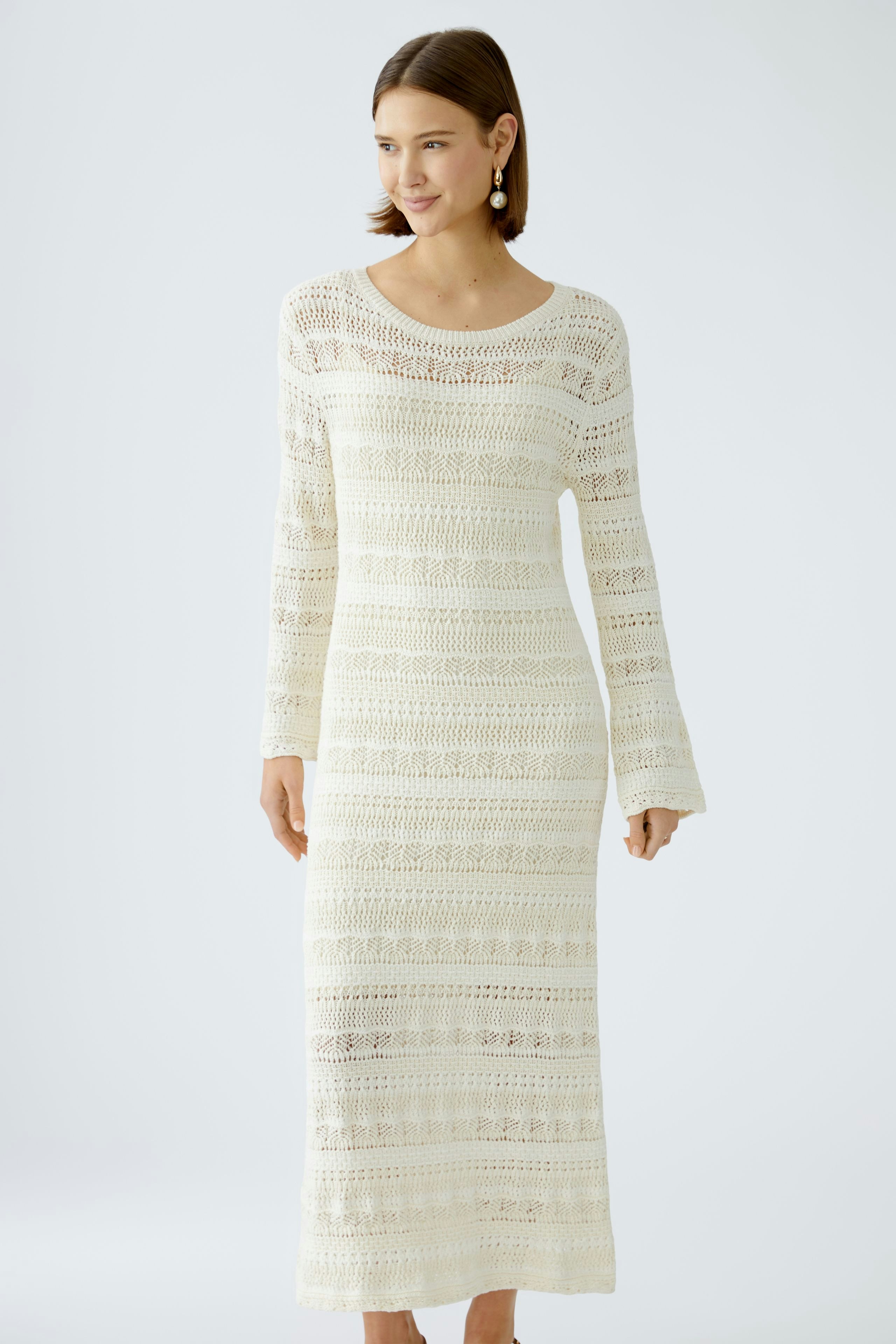 Elegantes Strickkleid: Frau in einem langen, weißen Strickkleid mit feinen Mustern und lässigem Schnitt.