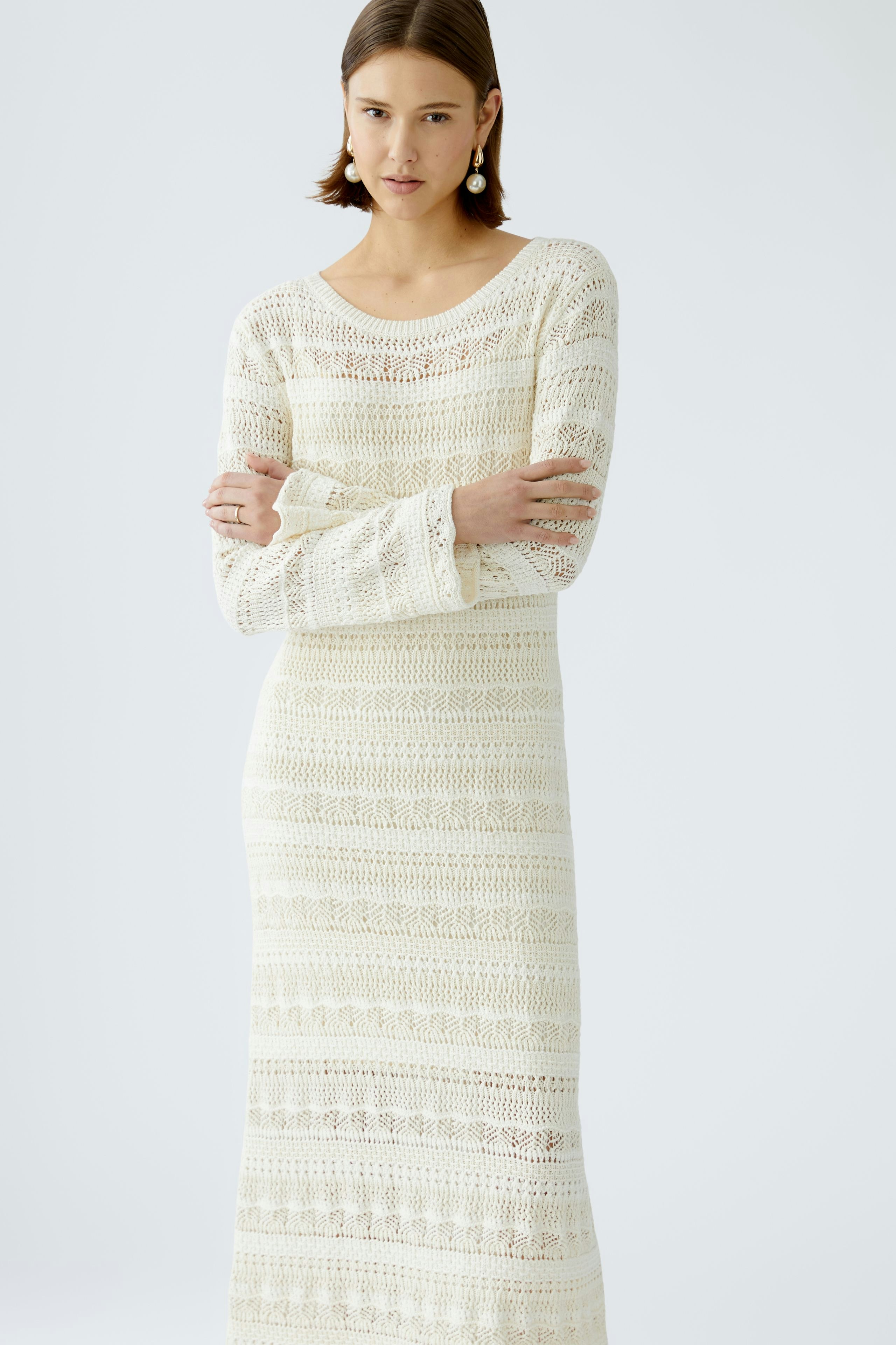 Elegantes Strickkleid: Frau in einem langen, weißen Strickkleid mit feinen Mustern und lässigem Schnitt.