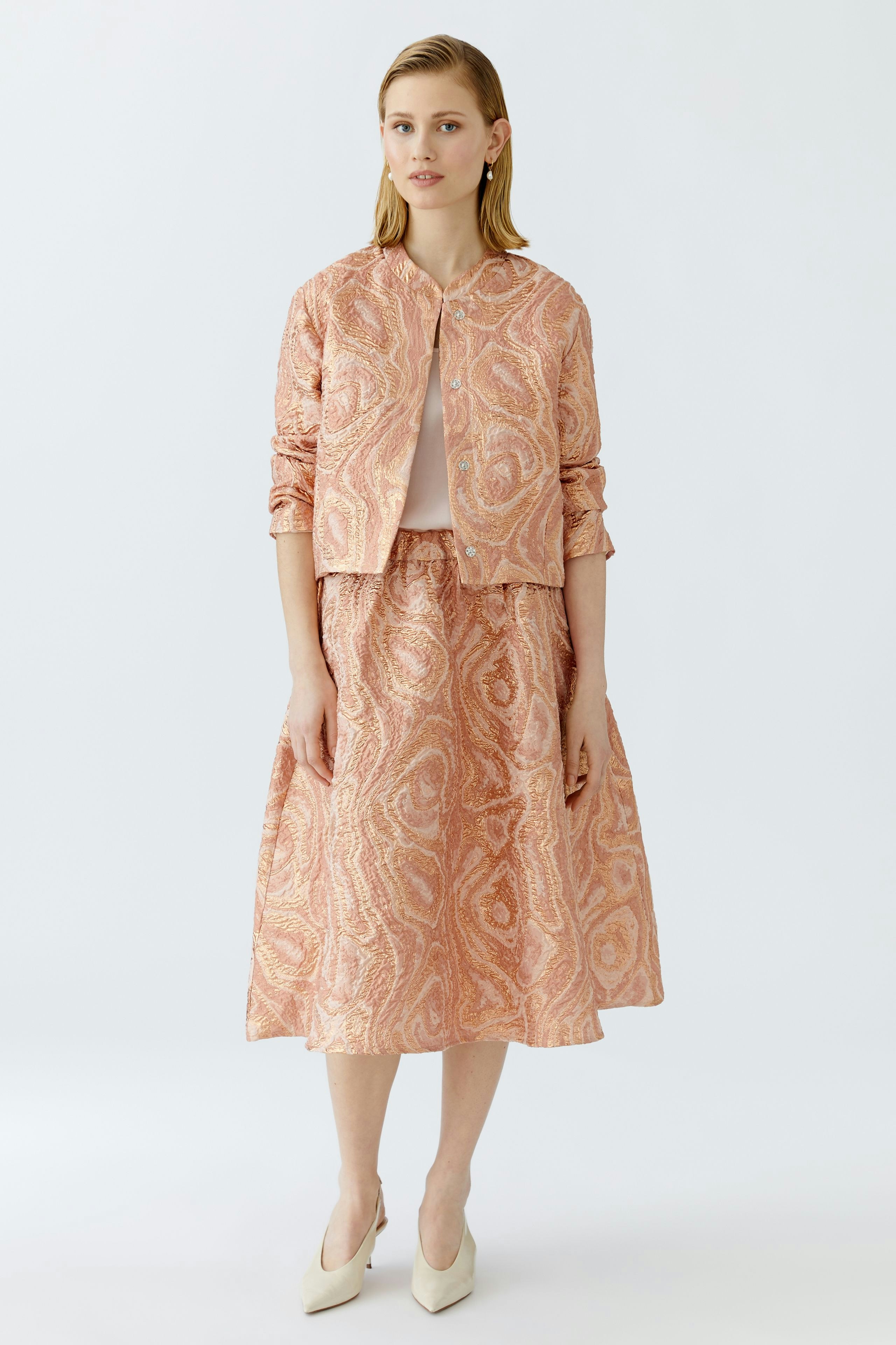 Eleganter Midirock: Junge Frau in einem gemusterten Midirock mit passender Jacke und eleganten Schuhen.