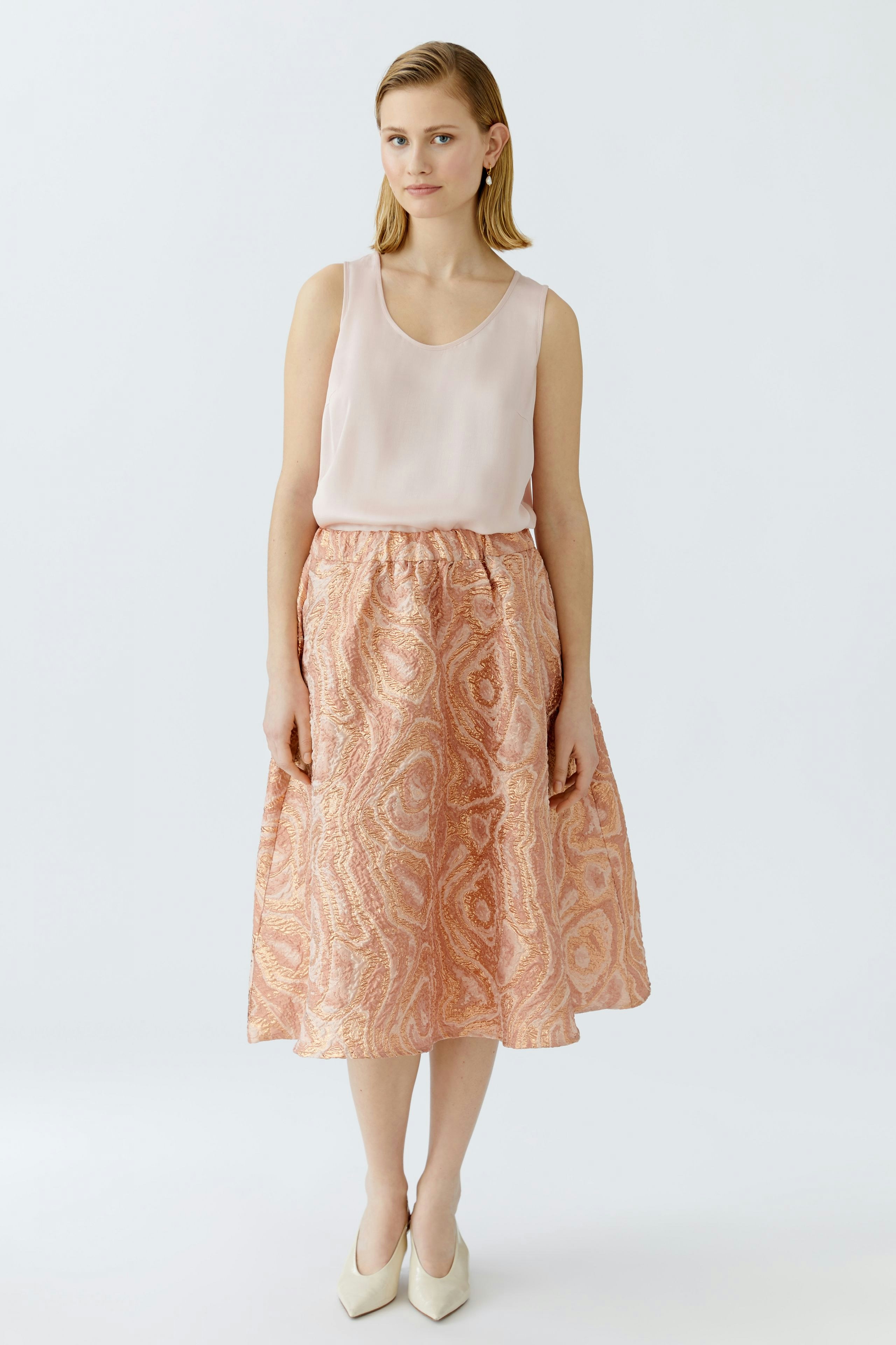 Eleganter Midirock: Junge Frau trägt einen rosafarbenen Midirock mit zartem Muster und lässigem Oberteil.