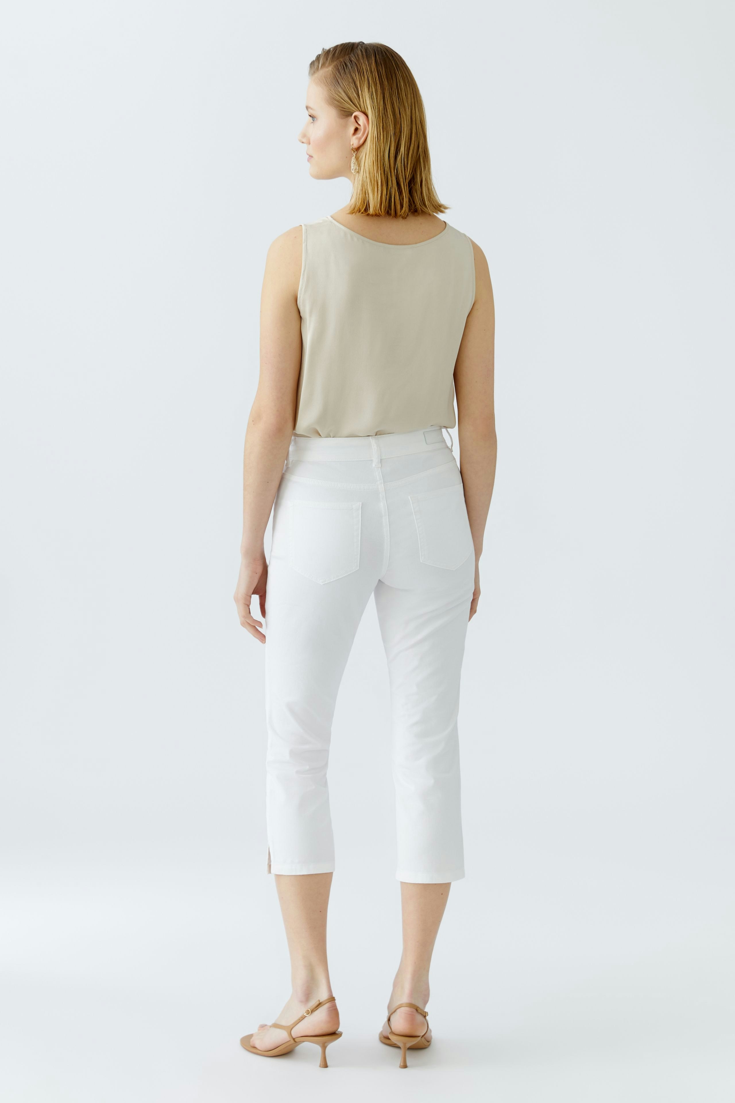 Stylish women's outfit: A woman in a beige top and white cropped pants, showcasing a chic look.
