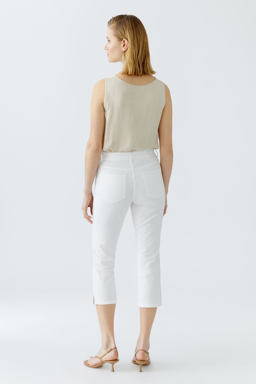 Stylish women's outfit: A woman in a beige top and white cropped pants, showcasing a chic look.