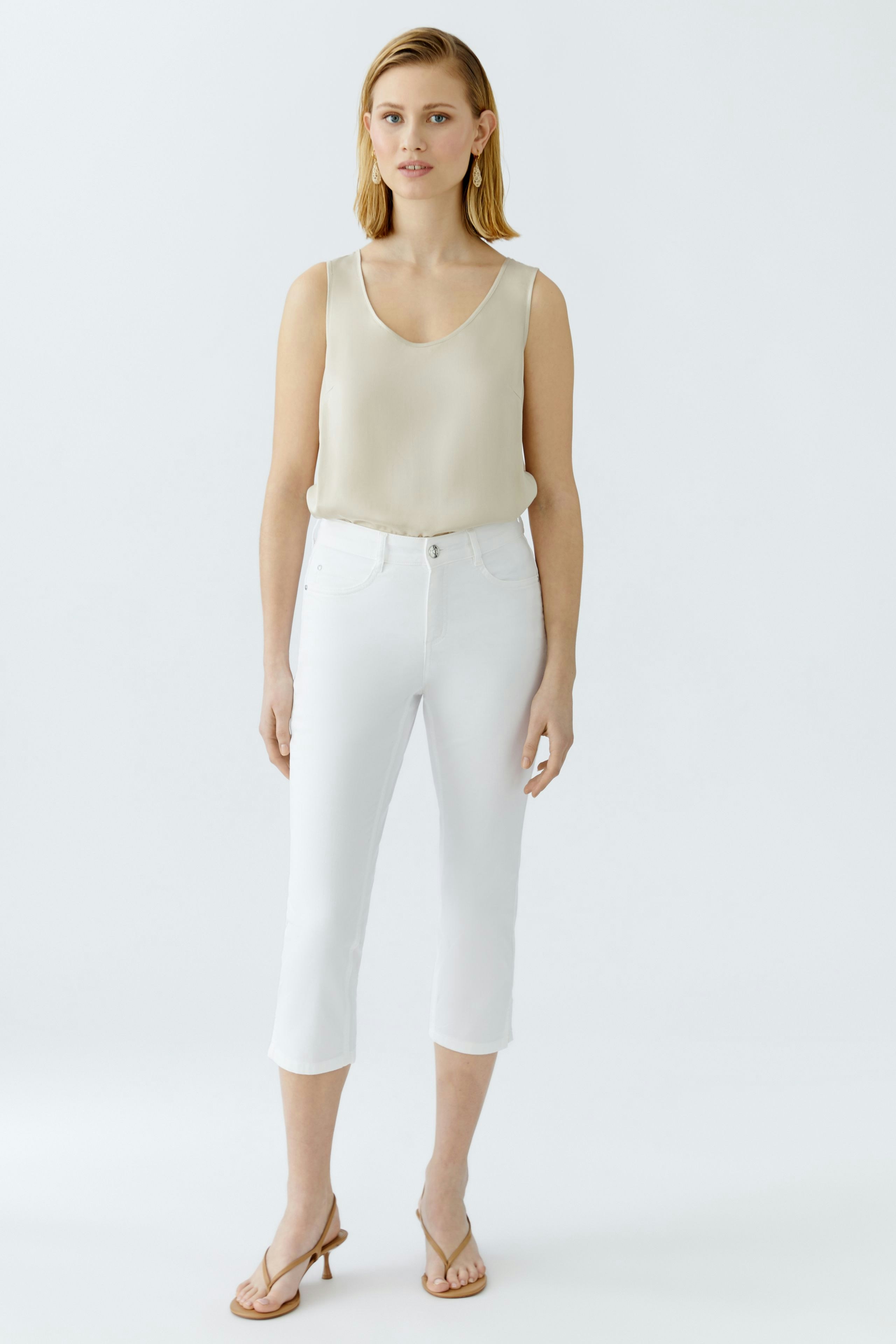 Elegant women's top: A woman in a light beige sleeveless top paired with white cropped pants.