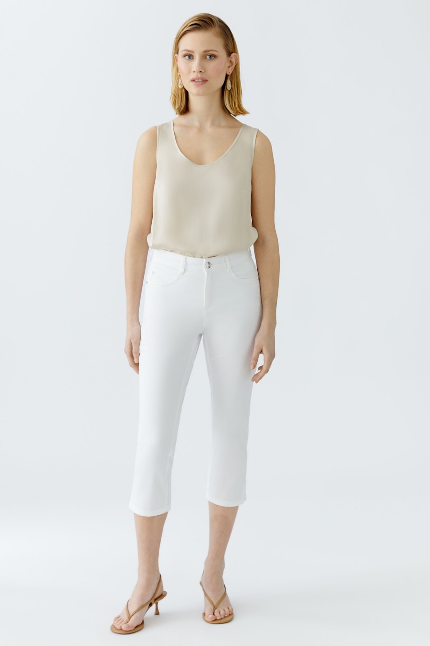 Elegant women's top: A woman in a light beige sleeveless top paired with white cropped pants.