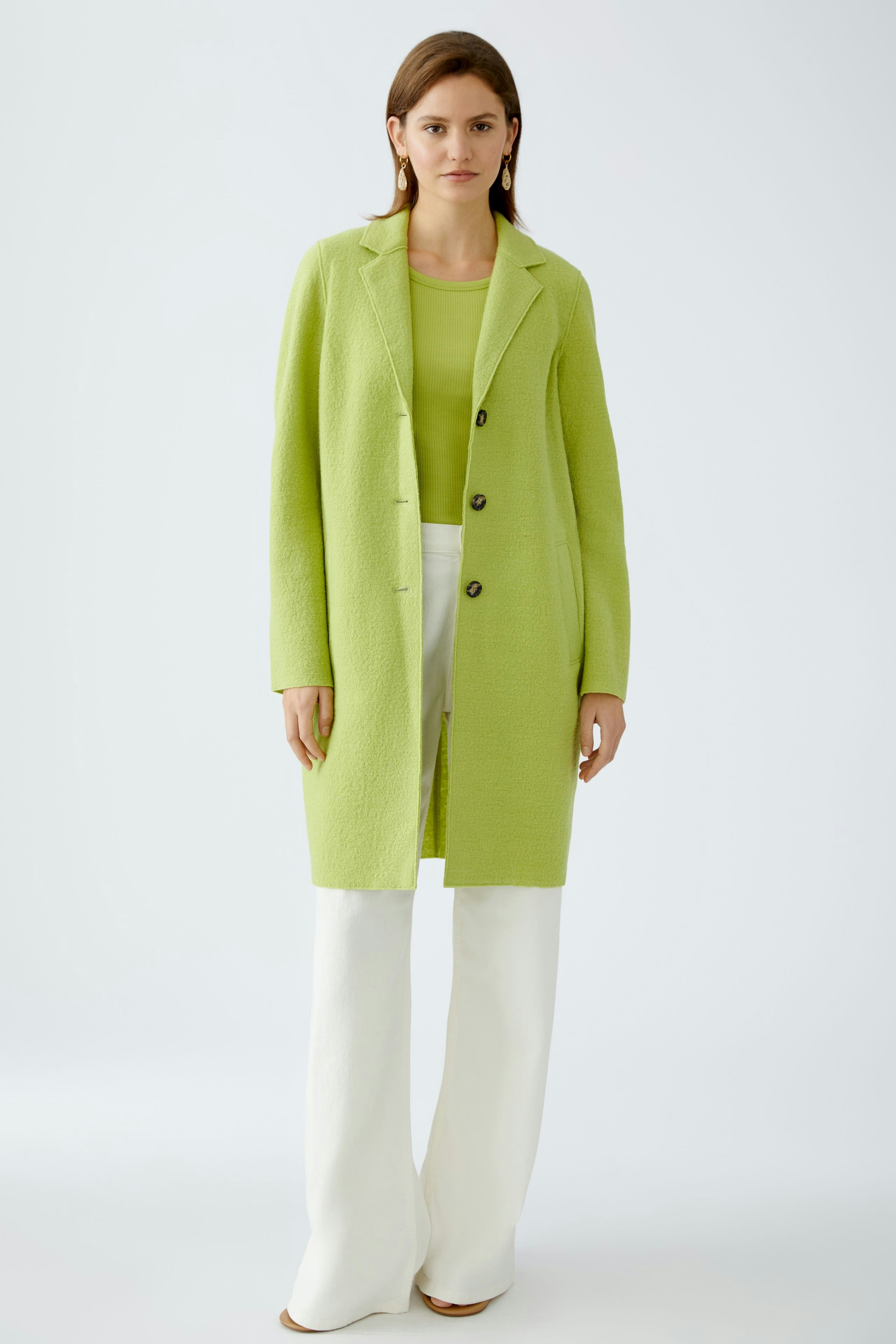Stylish women's wool coat in vibrant green, paired with a matching top and white trousers.