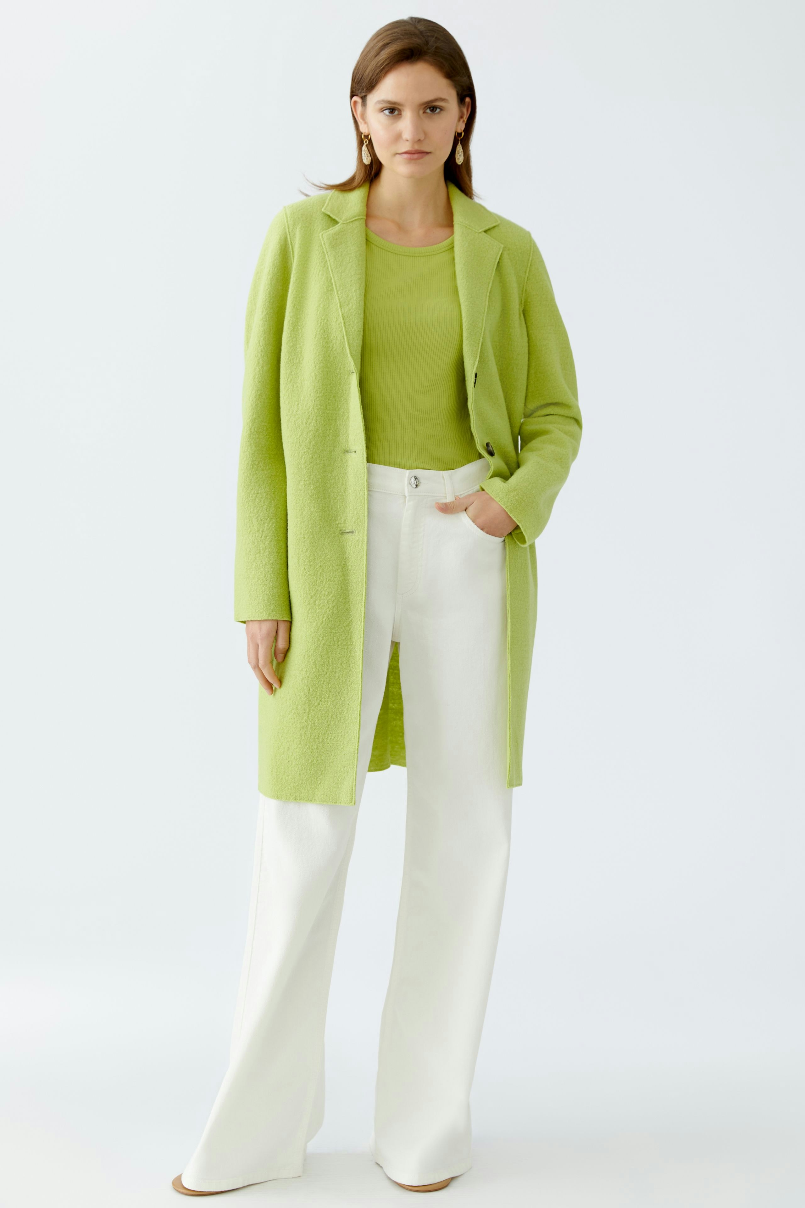 Chic women's wool coat: A woman in a vibrant green coat over a matching top and white pants.