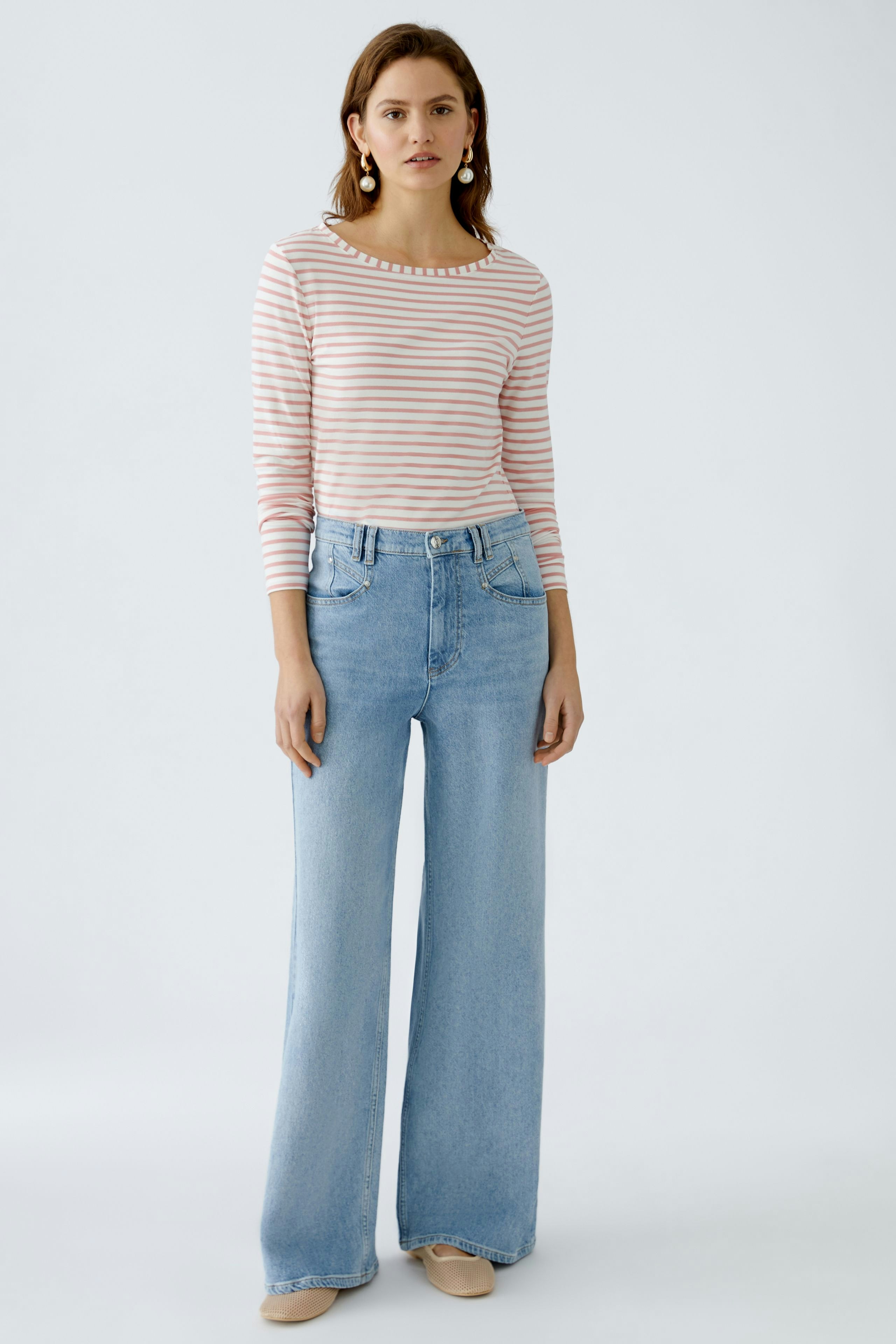 Langarmshirt: Junge Frau in gestreiftem Langarmshirt mit lässigen Jeans steht entspannt.