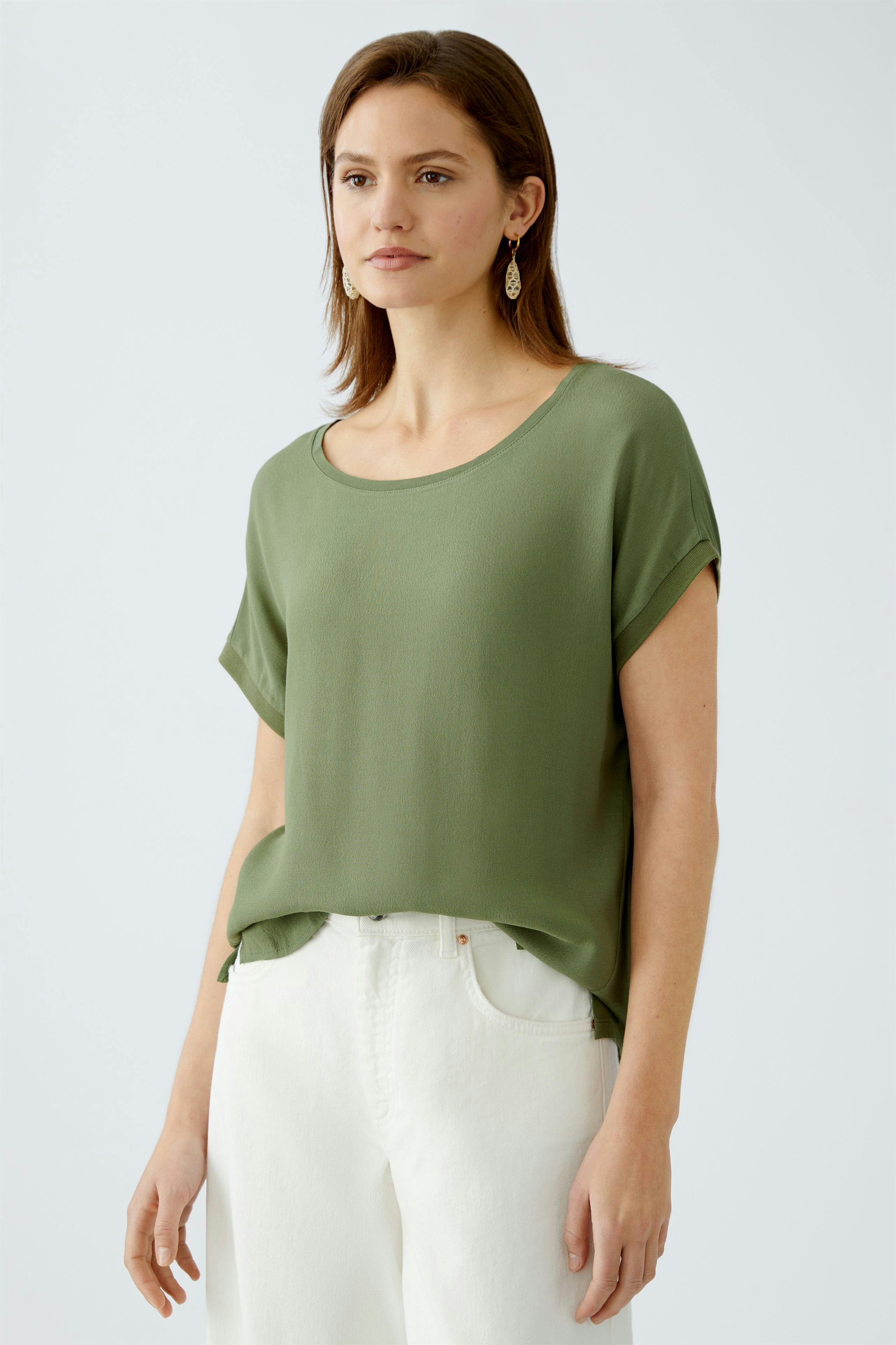 Blusenshirt: Frau trägt ein lässiges, grünes Blusenshirt mit kurzen Ärmeln und elegantem Schnitt.