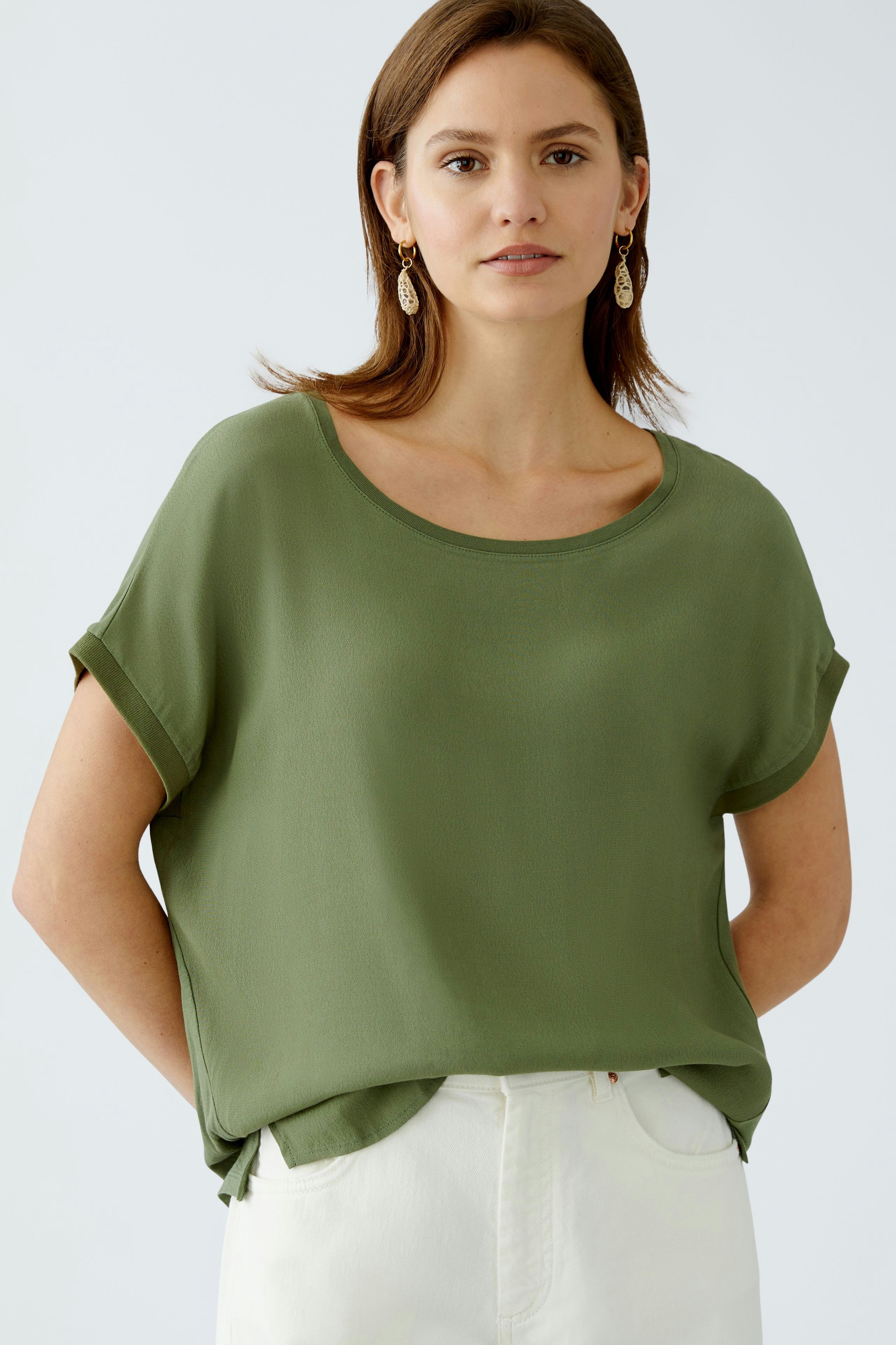 Luftiges Blusenshirt: Frau trägt ein olivgrünes, lässiges Blusenshirt mit kurzen Ärmeln.