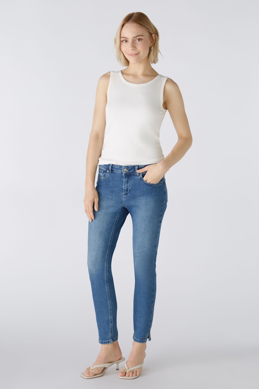 Stylish women's top: A woman in a white sleeveless top paired with blue jeans, exuding casual elegance.