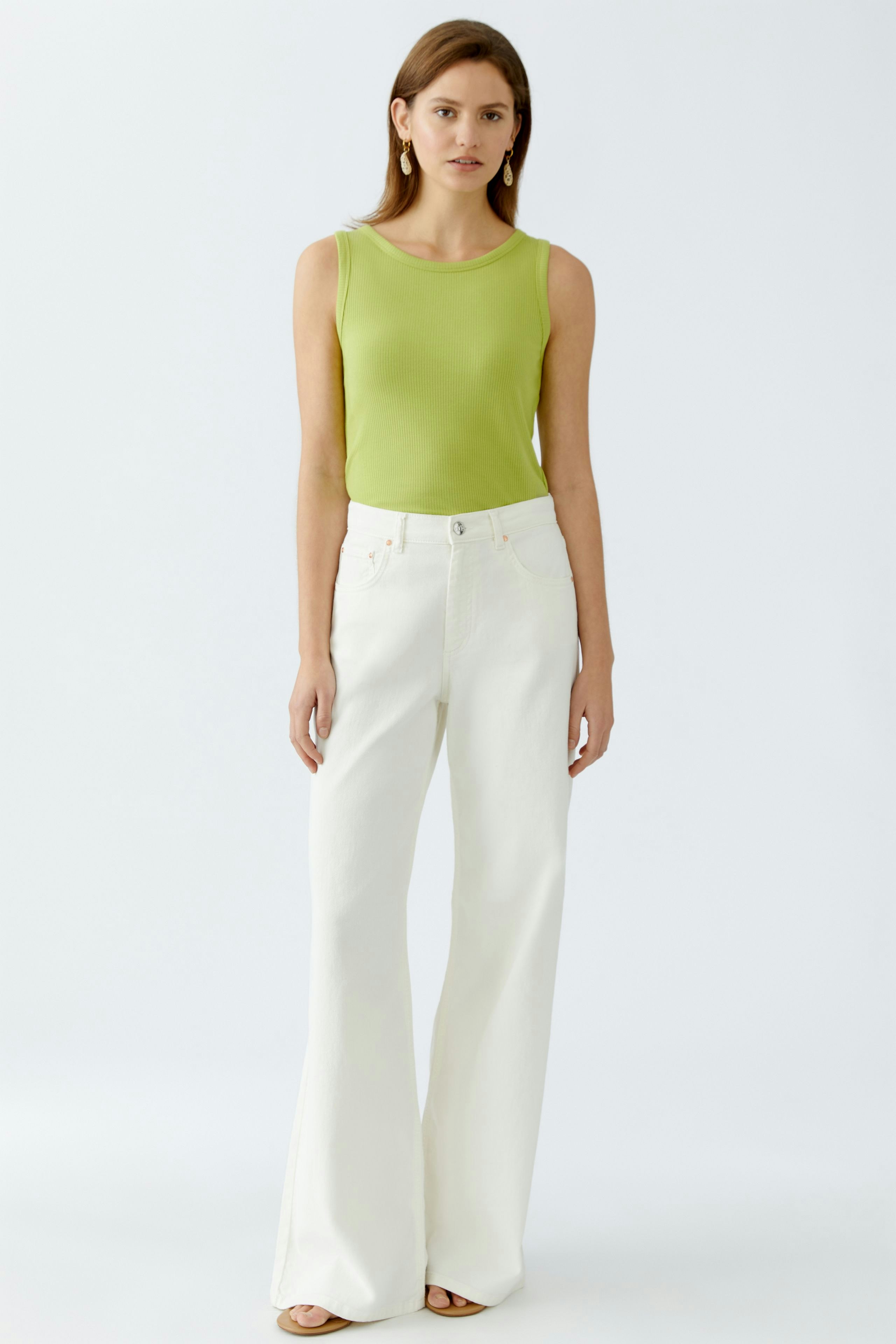 Damen-Top: Frau in grünem, ärmellosem Top und weißen, weiten Hosen steht selbstbewusst.