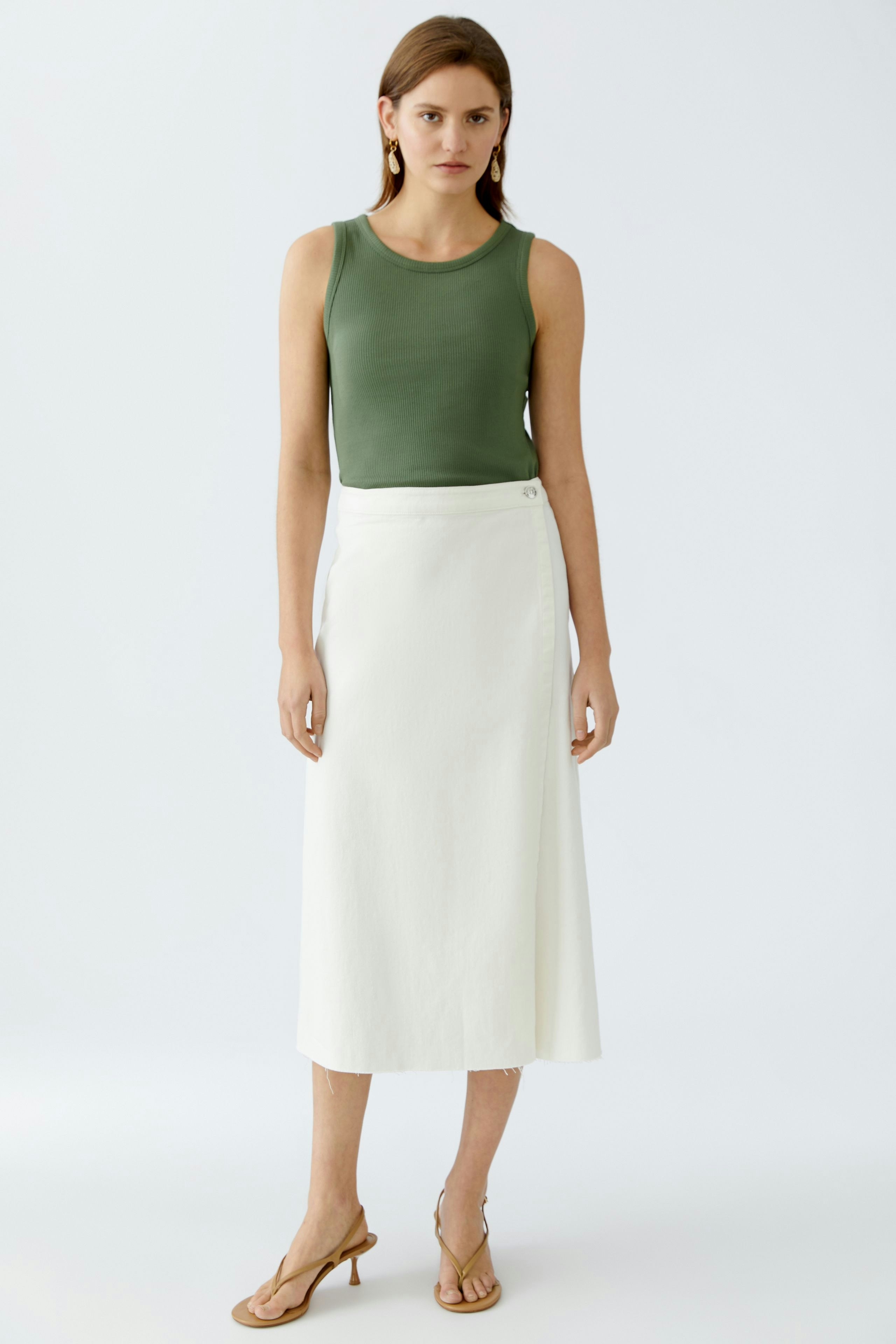 Stylish women's top: A woman in a green sleeveless top paired with a white skirt, exuding elegance.