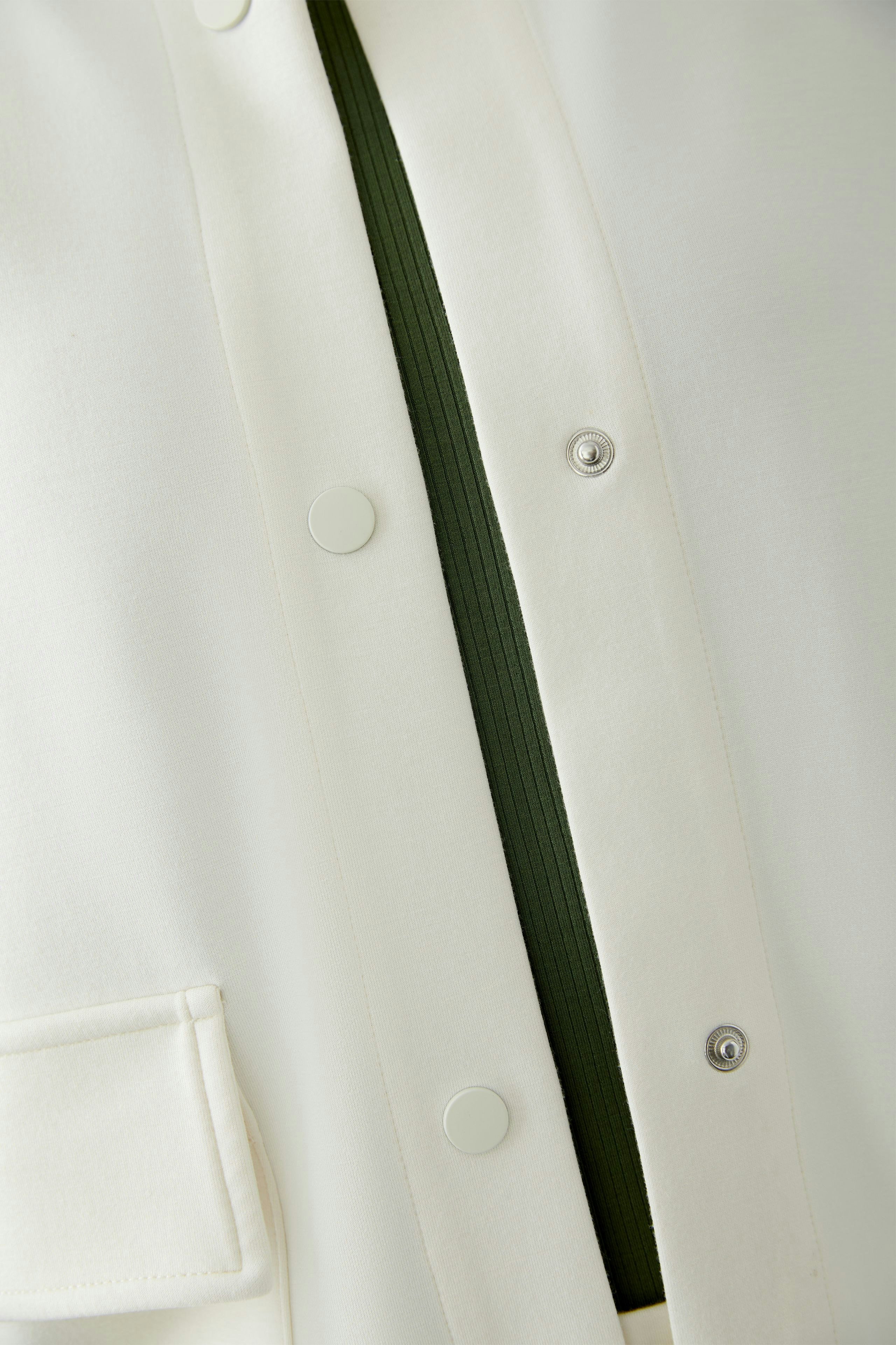 Eleganter Blouson: Weiße Jacke mit grünem Innenfutter und Druckknöpfen, ideal für stilvolle Outfits.