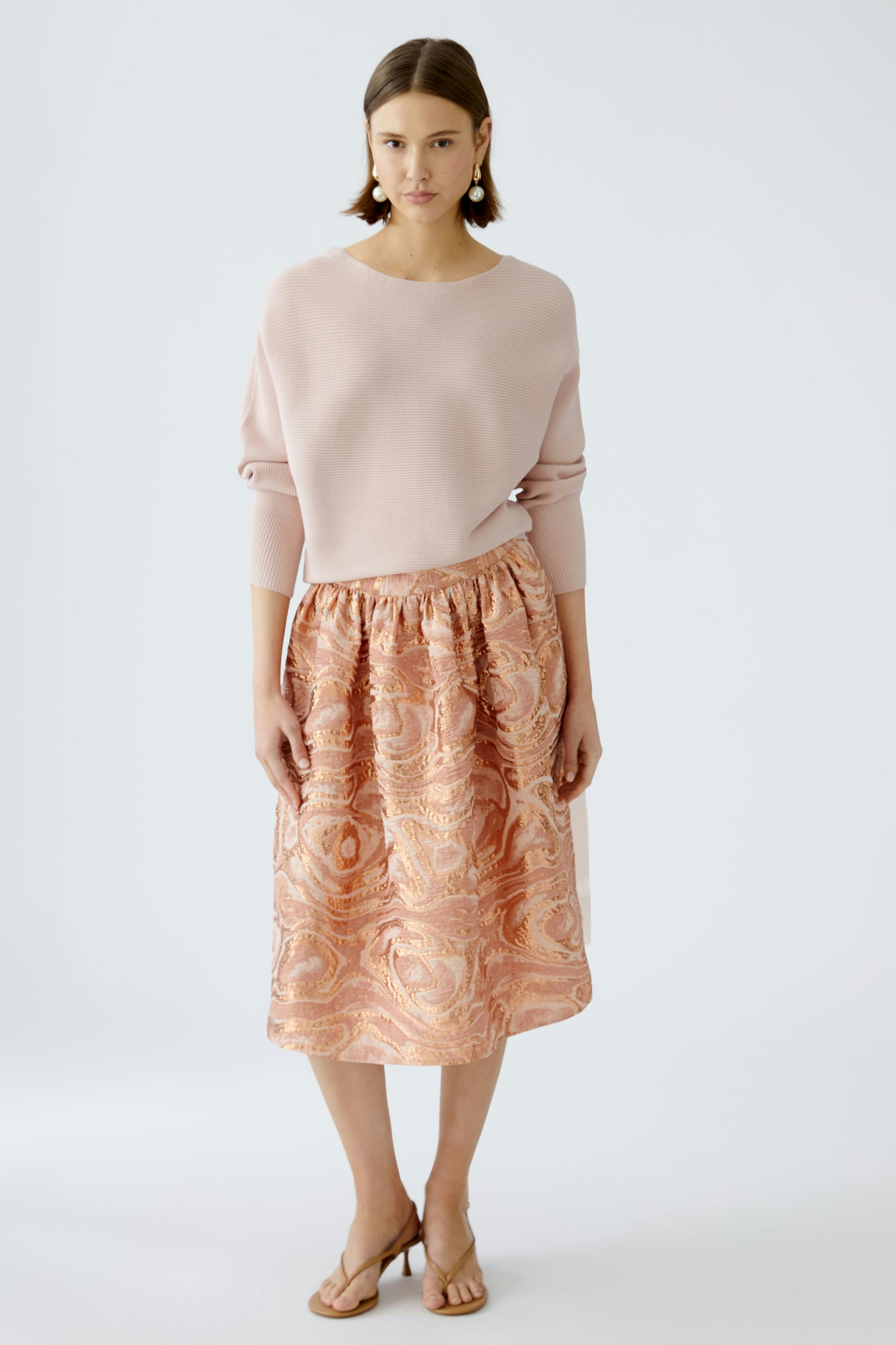 Eleganter Damen-Pullover in zartem Rosa, kombiniert mit einem gemusterten Rock für einen stilvollen Look.