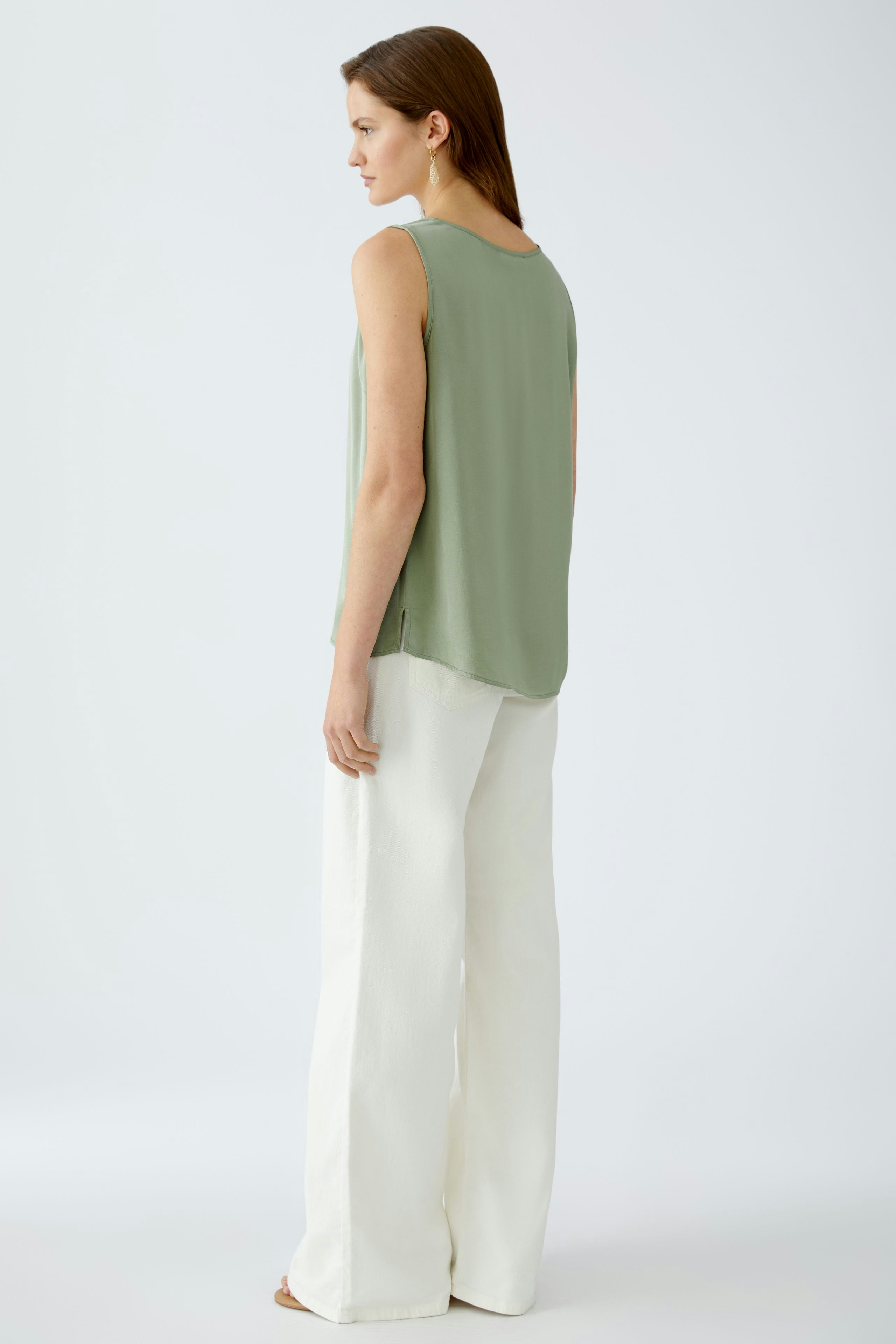 Elegantes Damen-Top in sanftem Grün, lässig kombiniert mit weißen, weiten Hosen.