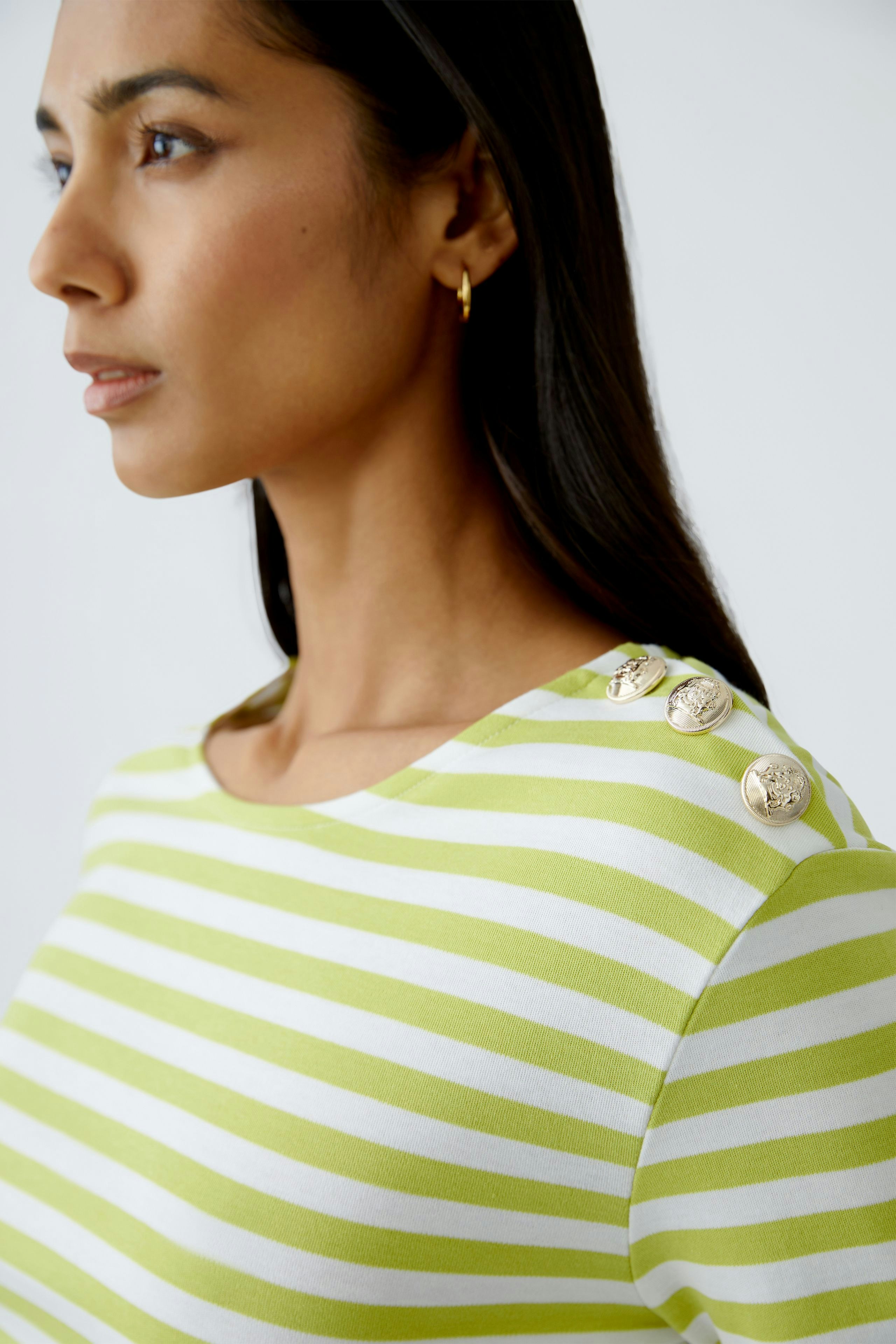 Stylish long-sleeve shirt: Woman in a green and white striped pullover with decorative buttons.