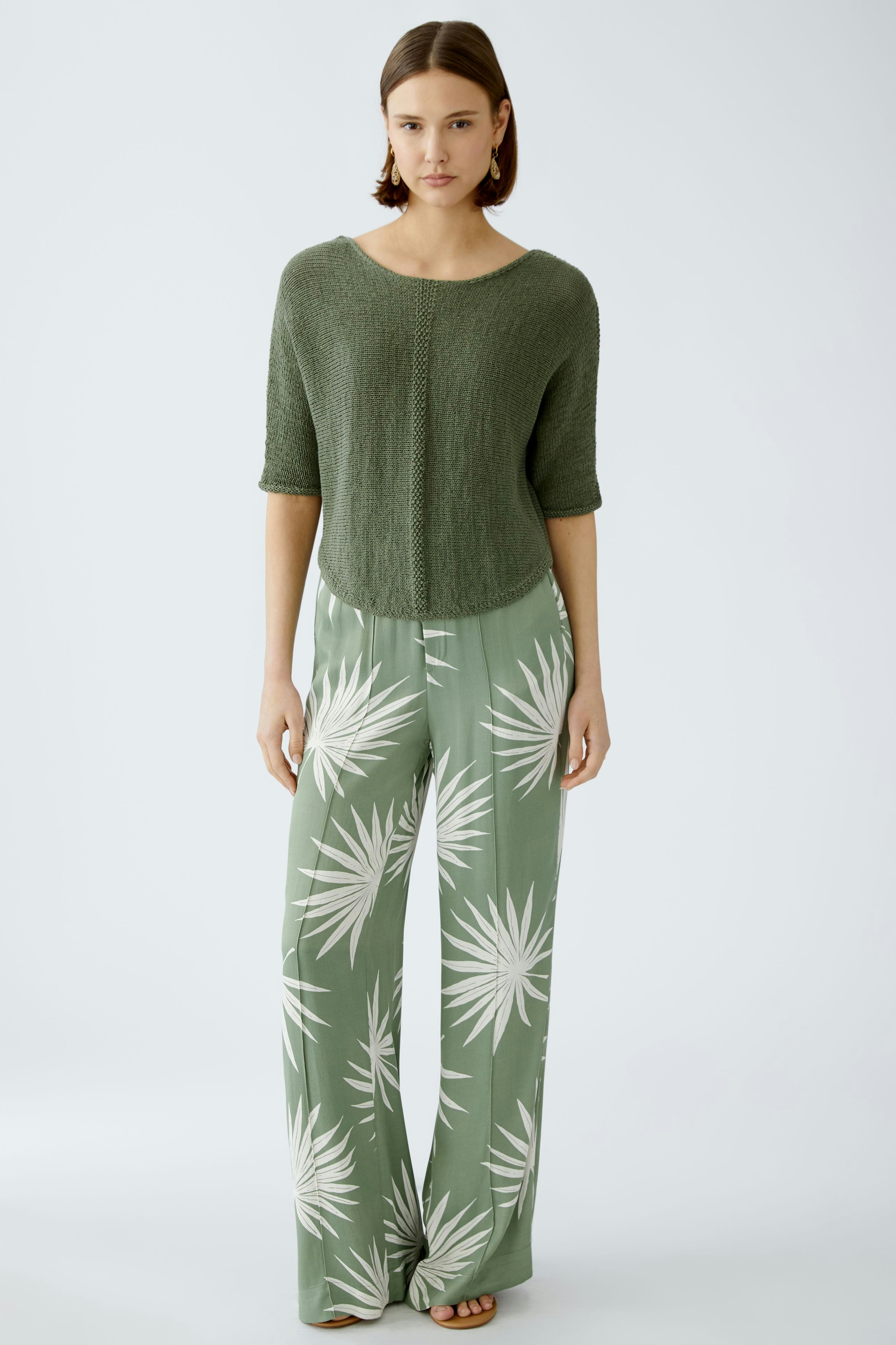 Moderne Damen-Hose: Frau in lässiger, grüner Hose mit Palmenmuster steht selbstbewusst.
