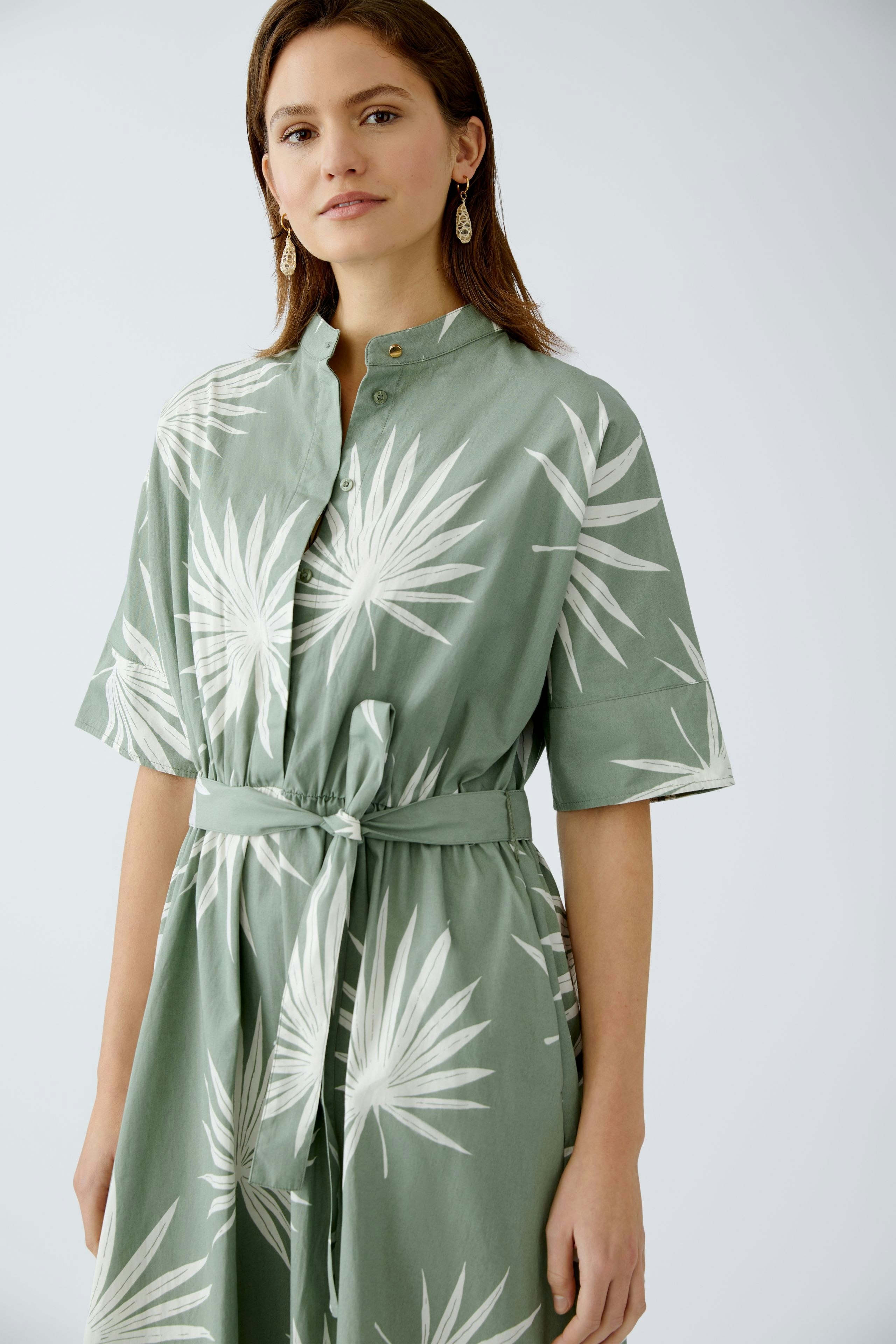 Elegantes Midikleid: Frau in grünem Kleid mit Palmenmuster und Gürtel, ideal für den Sommer.