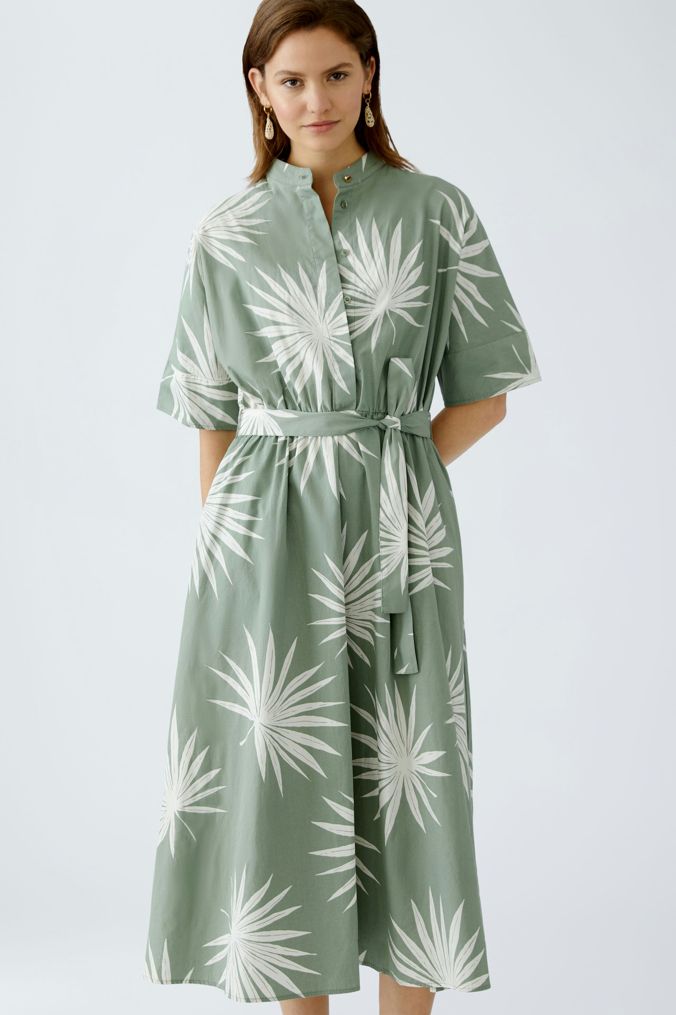 Elegantes Midikleid: Frau in grünem Kleid mit floralem Muster und Gürtel, ideal für den Sommer.