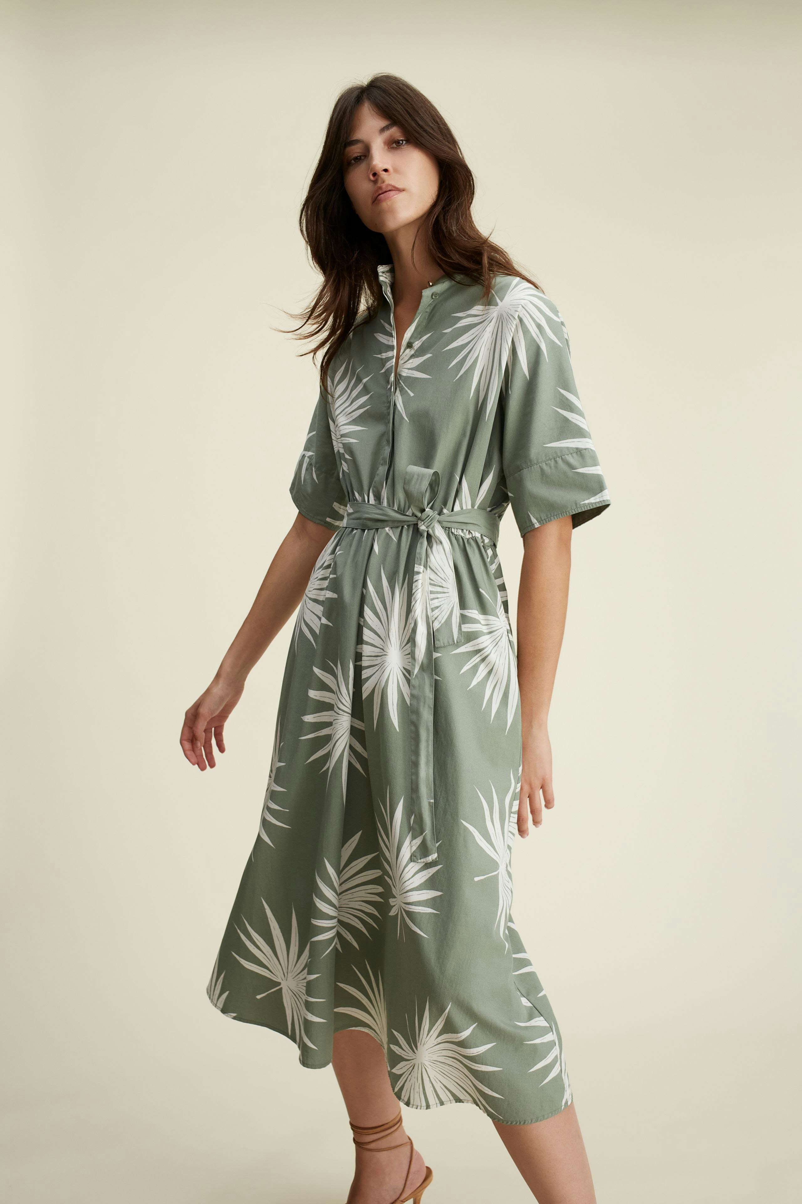 Elegantes Midikleid: Frau in grünem Kleid mit Palmenmuster, lässig und stilvoll.
