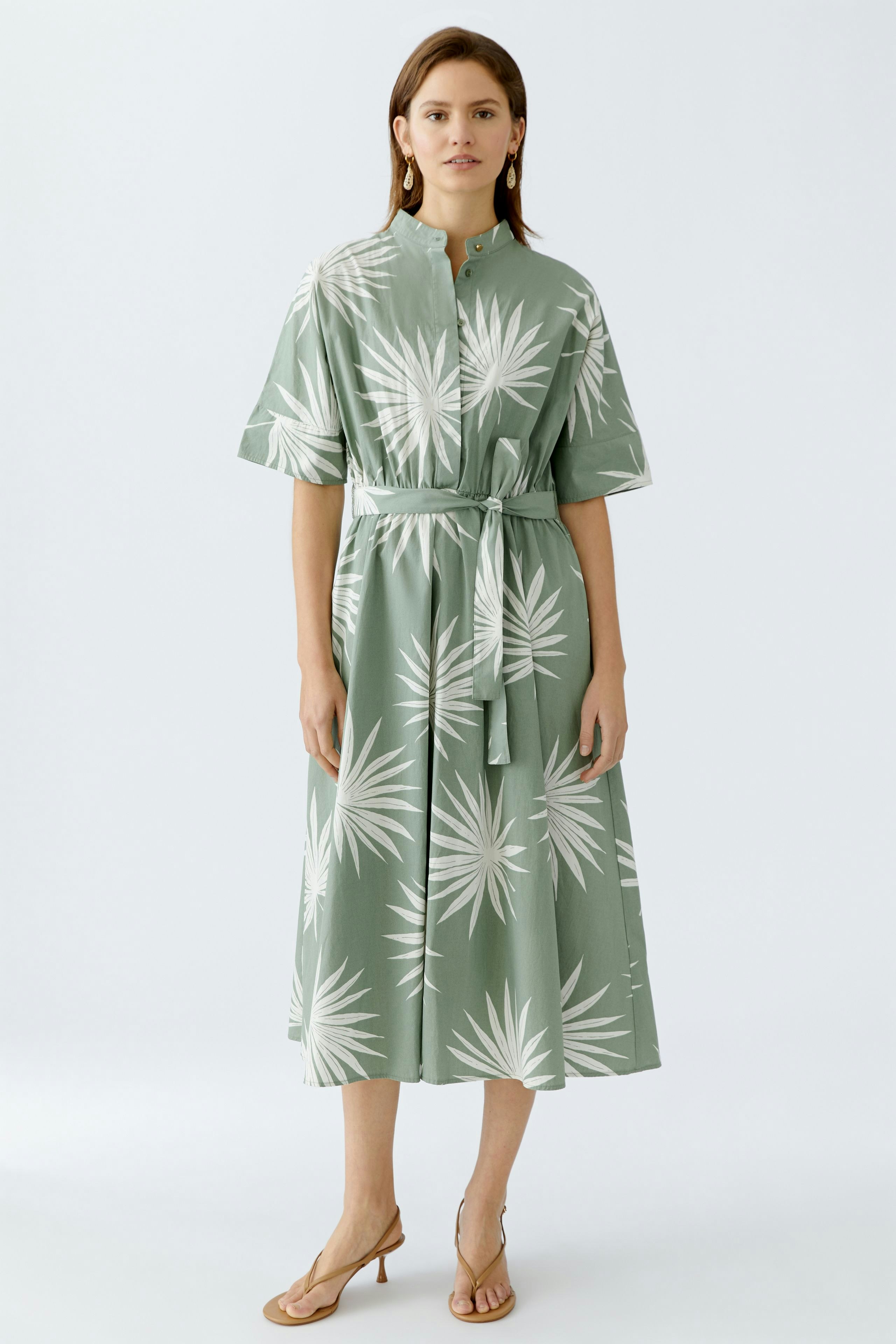 Elegantes Midikleid: Frau in grünem Kleid mit Palmblatt-Muster und Taillengürtel steht selbstbewusst.