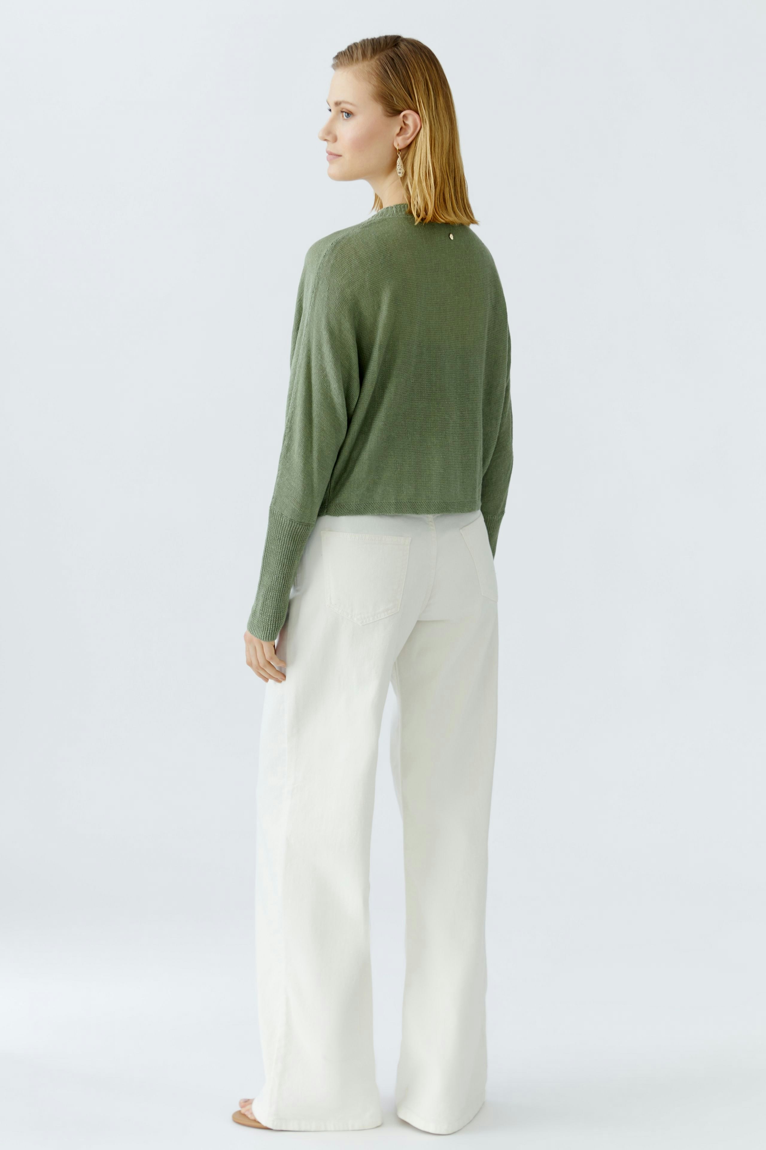 Damen-Strickjacke: Frau in grüner, lässiger Strickjacke mit weitem Schnitt und hellen Hosen.